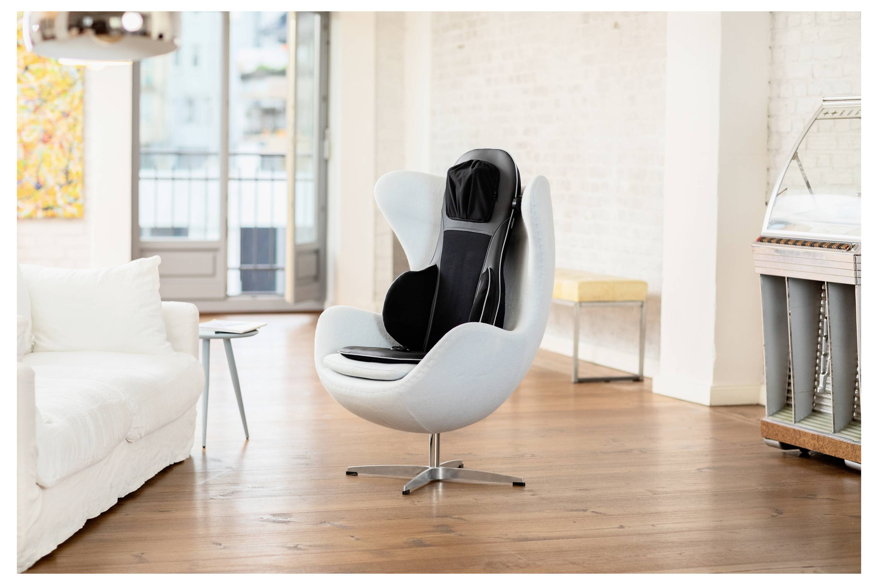 Un cuscinetto per seduta massaggiante dal design elegante è posizionato su una moderna sedia girevole bianca in un ambiente living contemporaneo e luminoso.