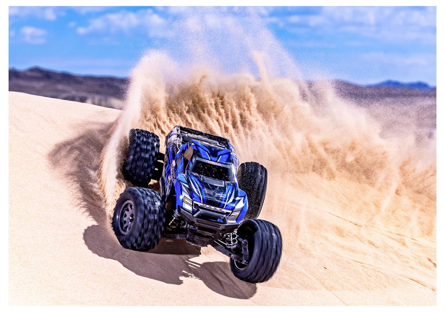 Un camion telecomandato solleva sabbia mentre corre giù per una duna desertica sotto un cielo azzurro terso.