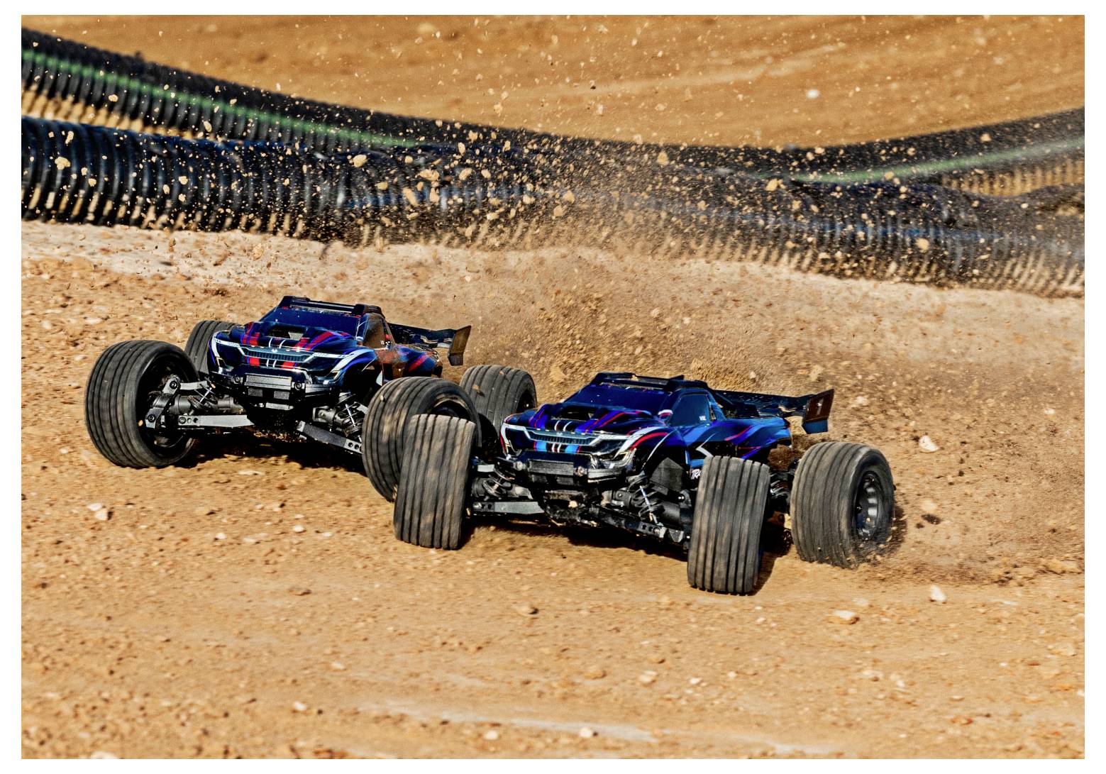 Due auto telecomandate gareggiano su una pista sterrata, sollevando polvere mentre affrontano una curva, mostrando velocità e manovrabilità.