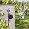 Un temporizzatore intelligente per l'acqua collegato a un rubinetto esterno controlla un tubo da giardino, innaffiando il prato sullo sfondo in una giornata di sole.
