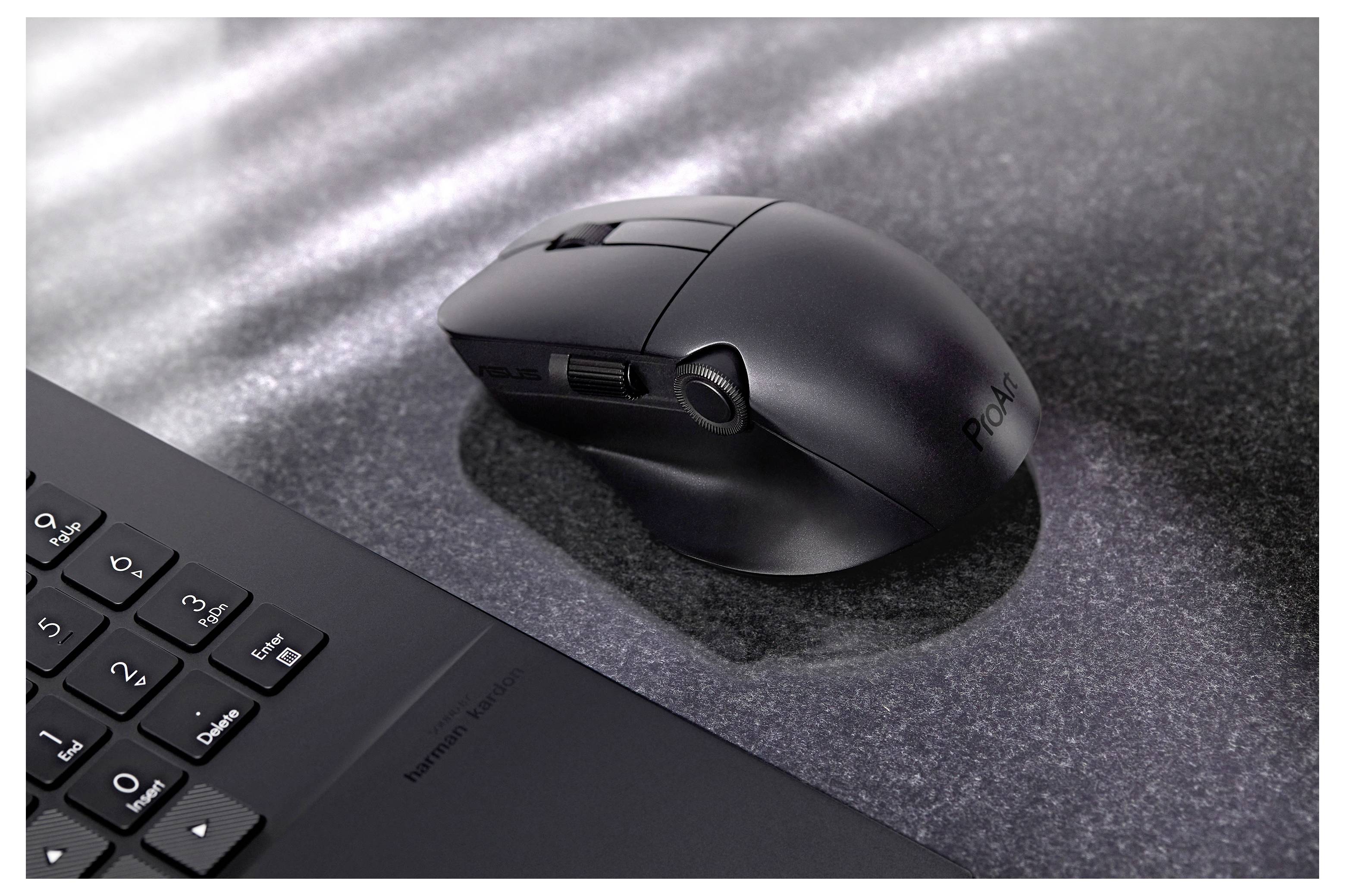 Un mouse wireless nero su una superficie testurizzata scura, accanto a una vista parziale di una tastiera di un laptop. La luce si diffonde attraverso la superficie.
