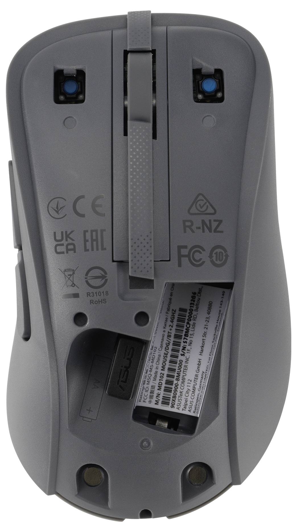 Il lato inferiore di un mouse per computer grigio che mostra loghi di certificazione, uno scomparto batterie aperto e un interruttore di accensione/spegnimento.