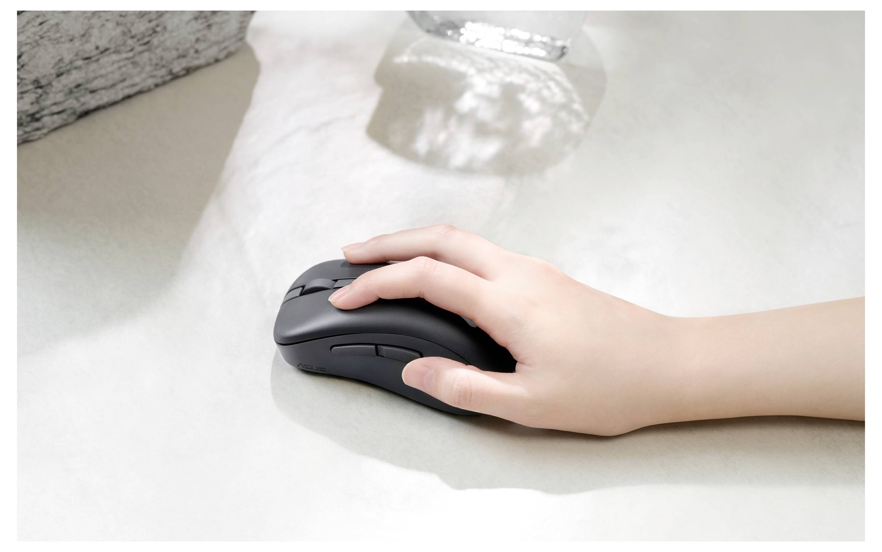 Una mano che utilizza un mouse nero per computer su una superficie chiara, con morbide ombre sullo sfondo.