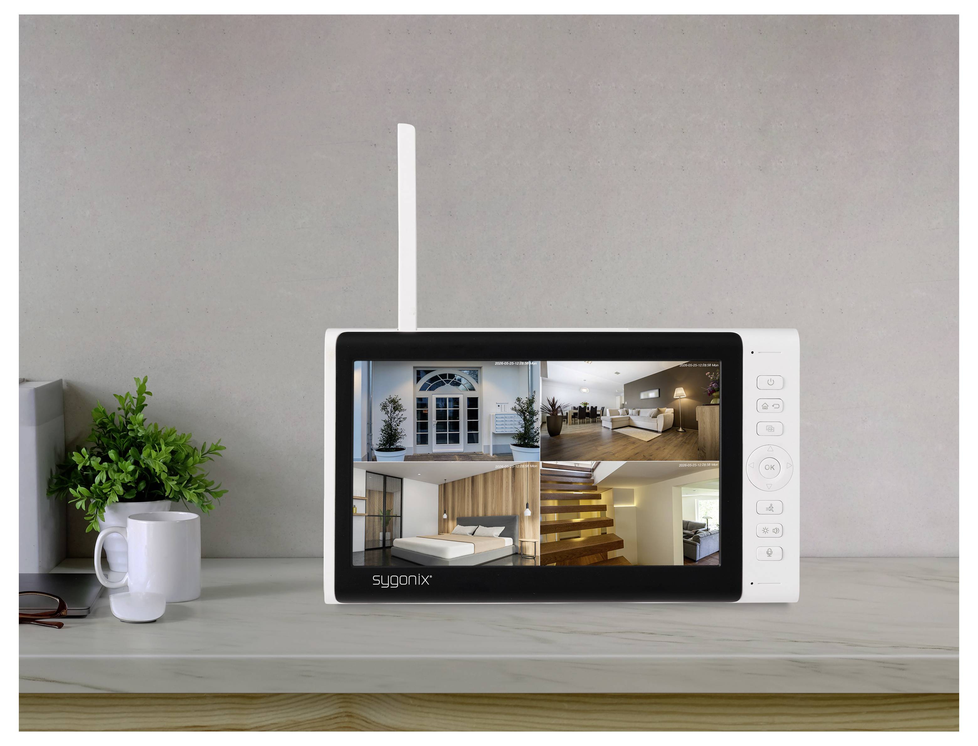 Monitor di sicurezza bianco su una scrivania che visualizza quattro viste di telecamere domestiche, con una pianta e una tazza accanto.