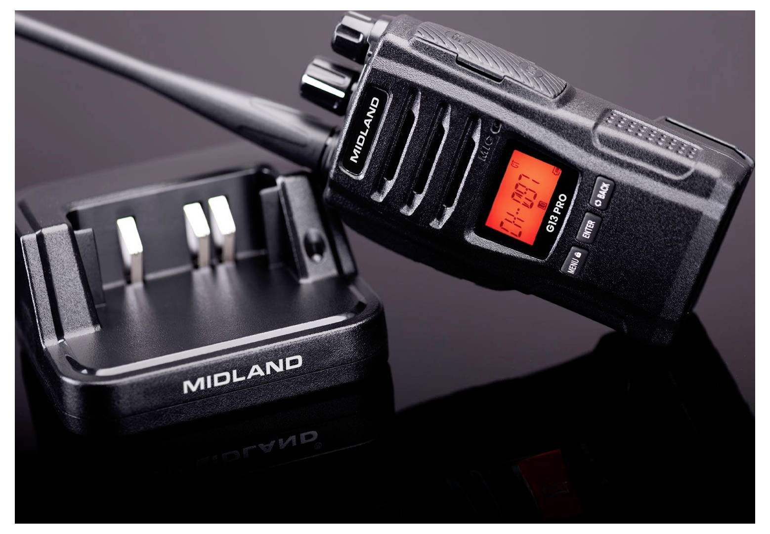 Un walkie-talkie Midland nero con schermo rosso che mostra 'CH-01', posizionato accanto a una base di ricarica nera, entrambi su una superficie lucida.