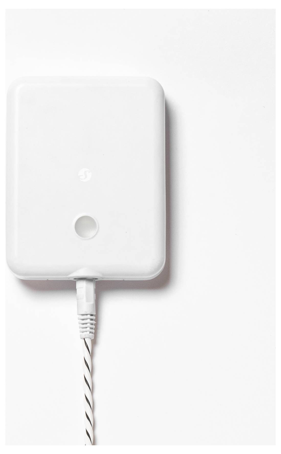 Dispositivo elettrico rettangolare bianco con un pulsante circolare, collegato da un cavo bianco su uno sfondo bianco uniforme.