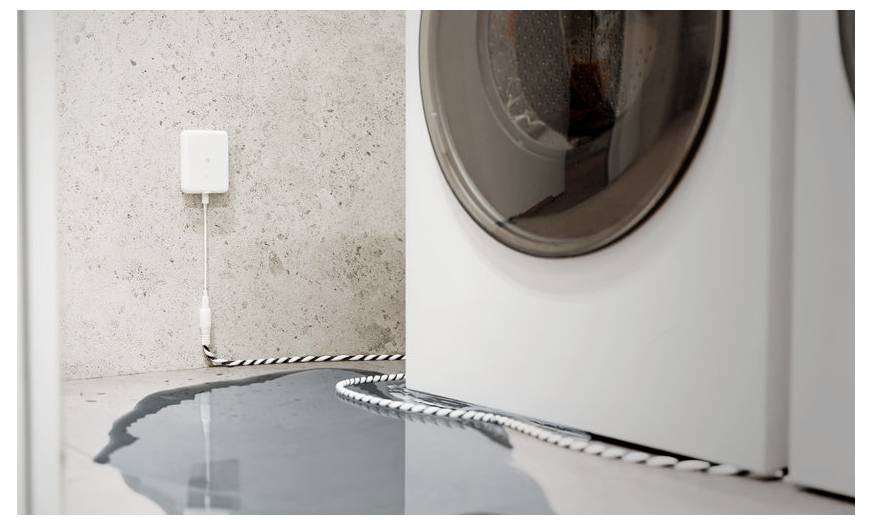 Una lavatrice a carica frontale perde acqua sul pavimento. Un sensore di acqua viene posizionato nelle vicinanze.