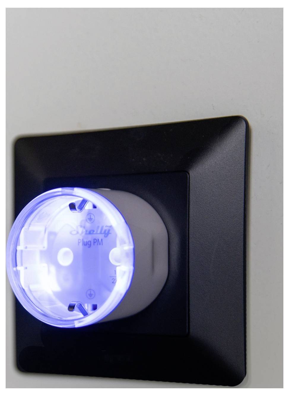 Una presa intelligente con una luce LED blu, collegata a una presa a muro, che indica una connessione di alimentazione attiva.
