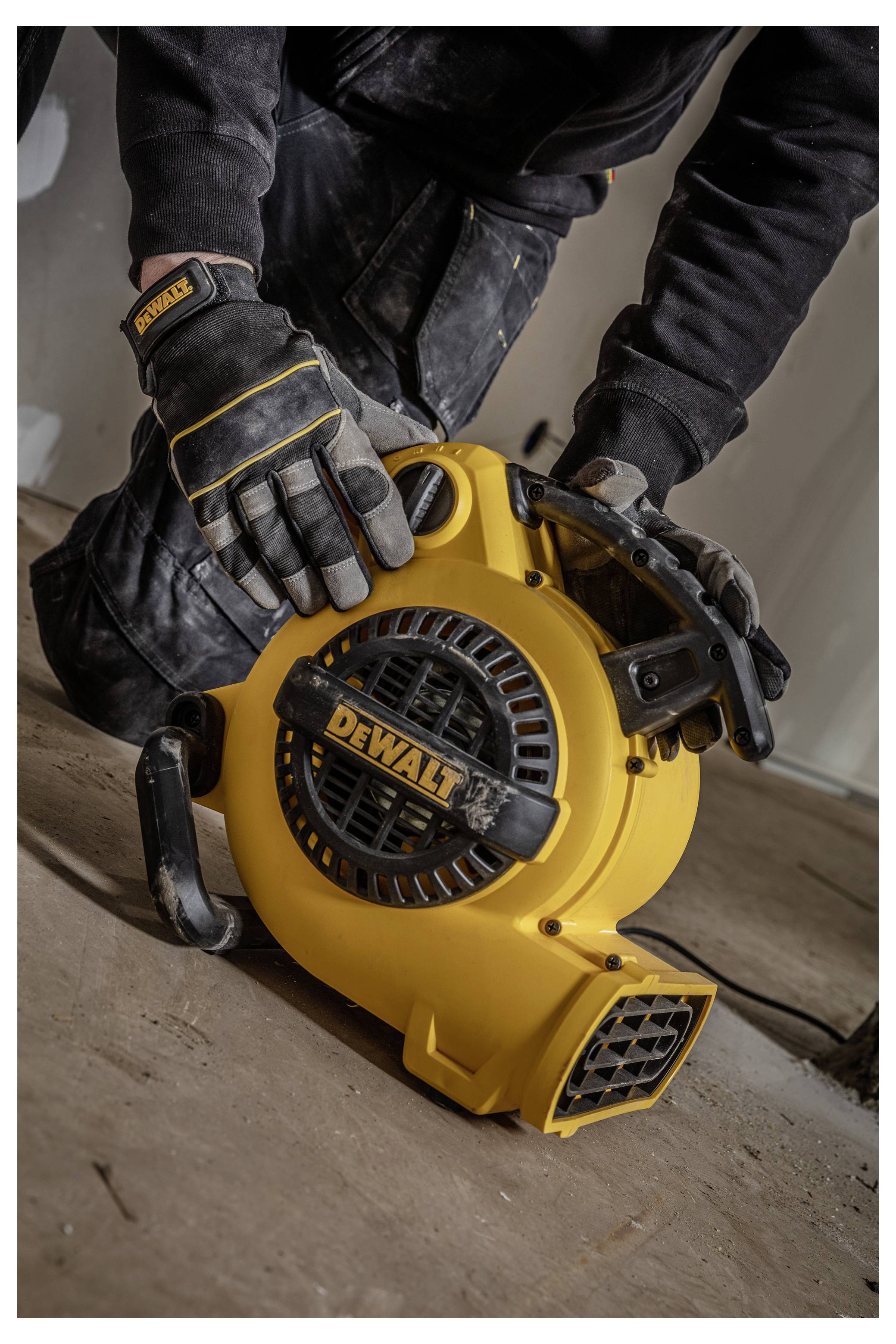 Operaio con guanti che maneggia un soffiatore portatile giallo DEWALT su un pavimento polveroso durante lavori di pulizia o costruzione.