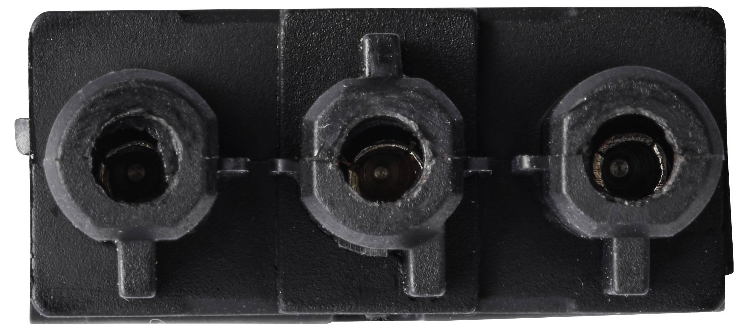 Primo piano di un connettore elettrico nero a tre porte o blocco di prese con aperture circolari in fila.