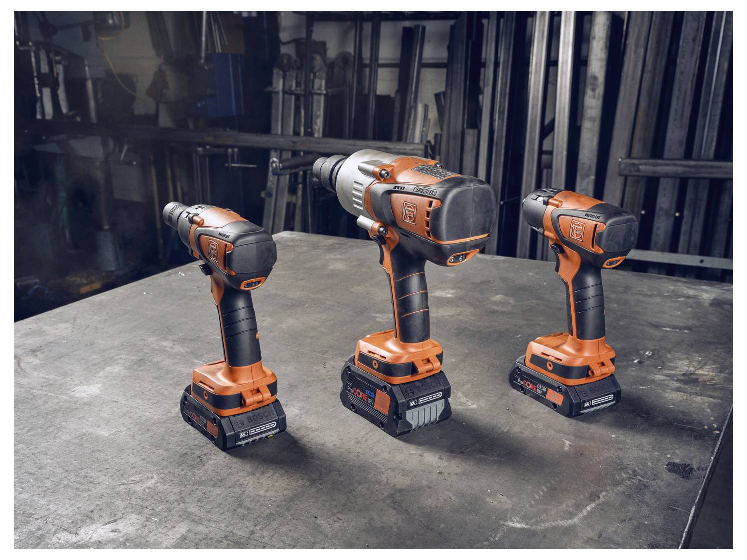 Tre trapani cordless sono esposti su un banco di lavoro in un'officina, evidenziando il loro design ergonomico e gli accenti arancioni.