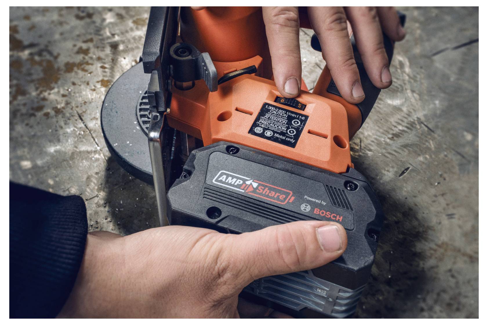 Una persona preme un pulsante su un attrezzo elettrico con il logo Bosch. Un'altra mano tiene saldo l'attrezzo su una superficie ruvida.