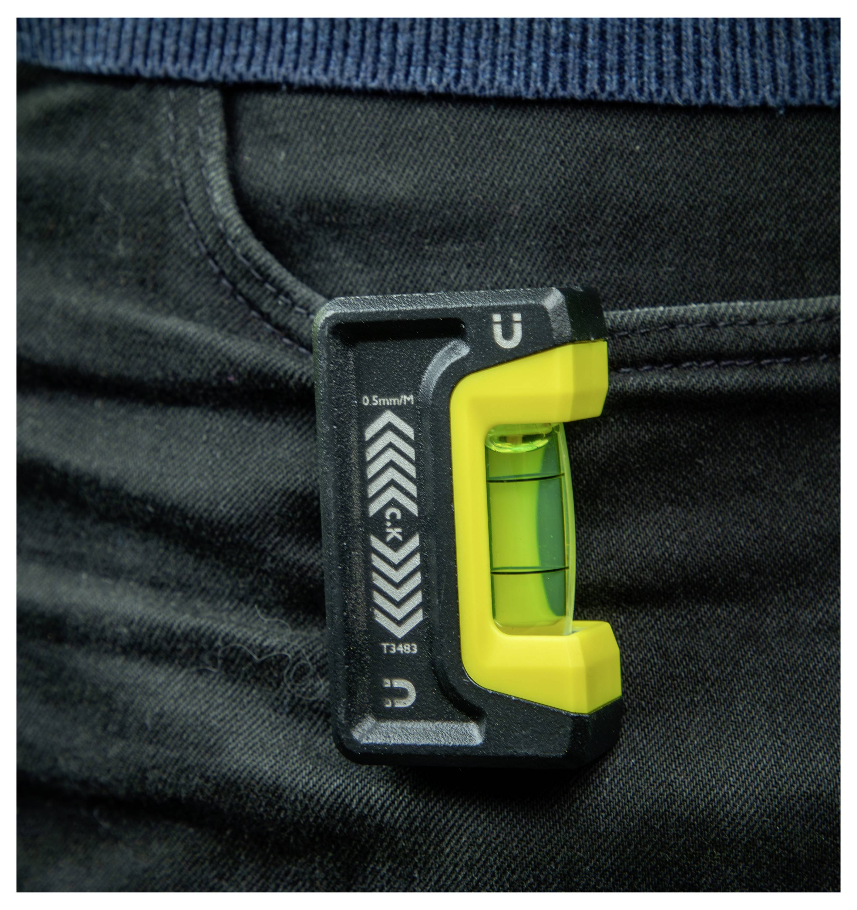 Un piccolo strumento a livella a bolla d'aria, di colore verde, a forma di U, attaccato a una tasca di denim nero.