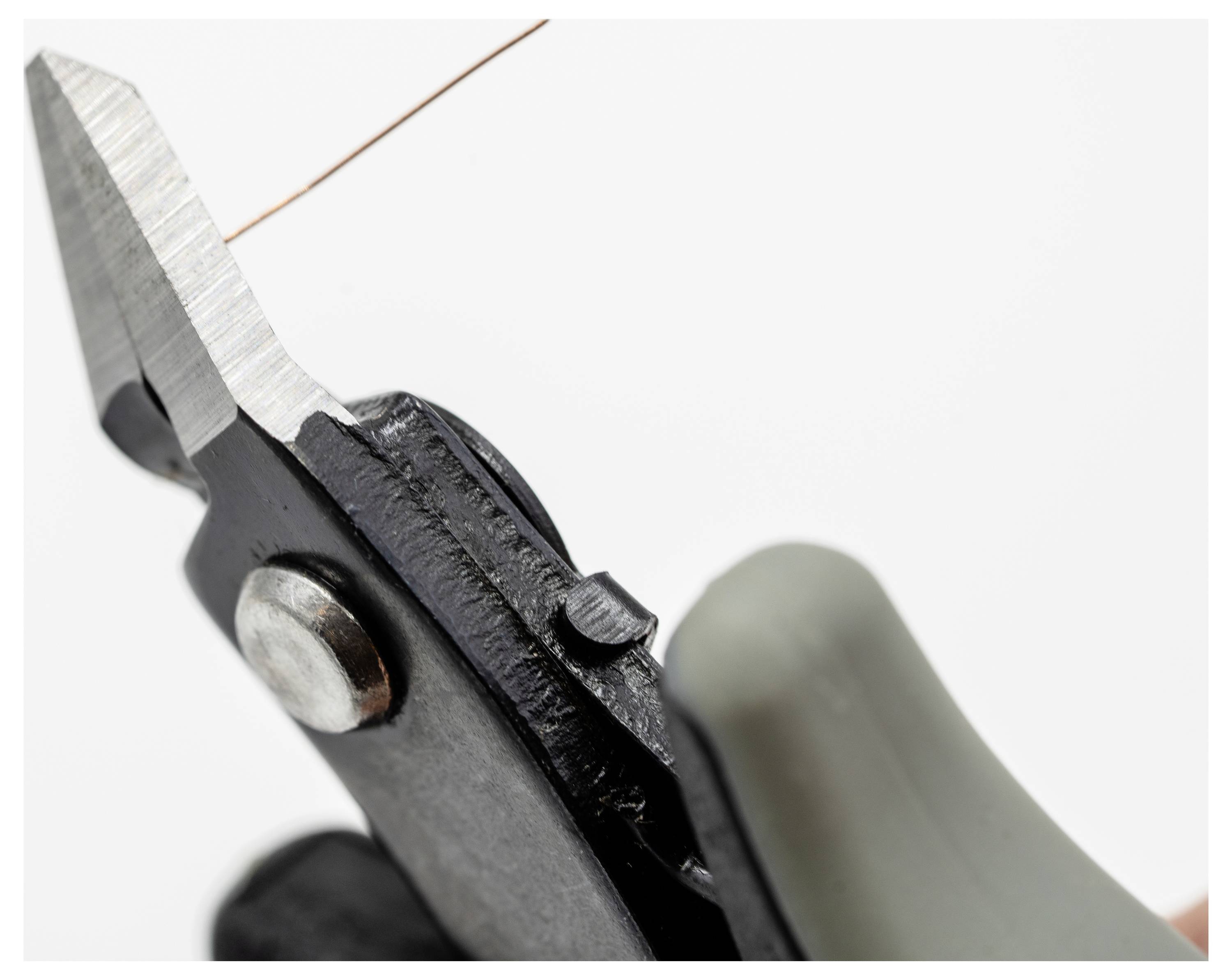 Una mano che regge tronchesi mentre taglia un sottile filo di rame su uno sfondo uniforme.