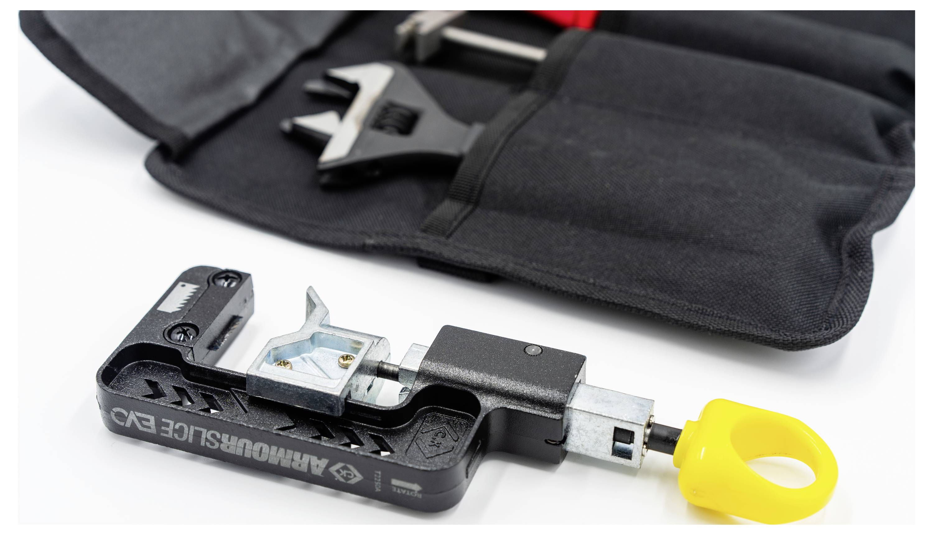 Un primo piano di uno strumento 'Armorlok Slide EXS' con un manico a anello giallo, posizionato su una borsa per attrezzi in tessuto nero con una chiave inglese visibile.