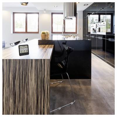 Una moderna cucina con un'isola con motivo legno e uno sgabello da bar nero. Un orologio digitale visualizza l'ora e la data. Le grandi finestre forniscono luce naturale.