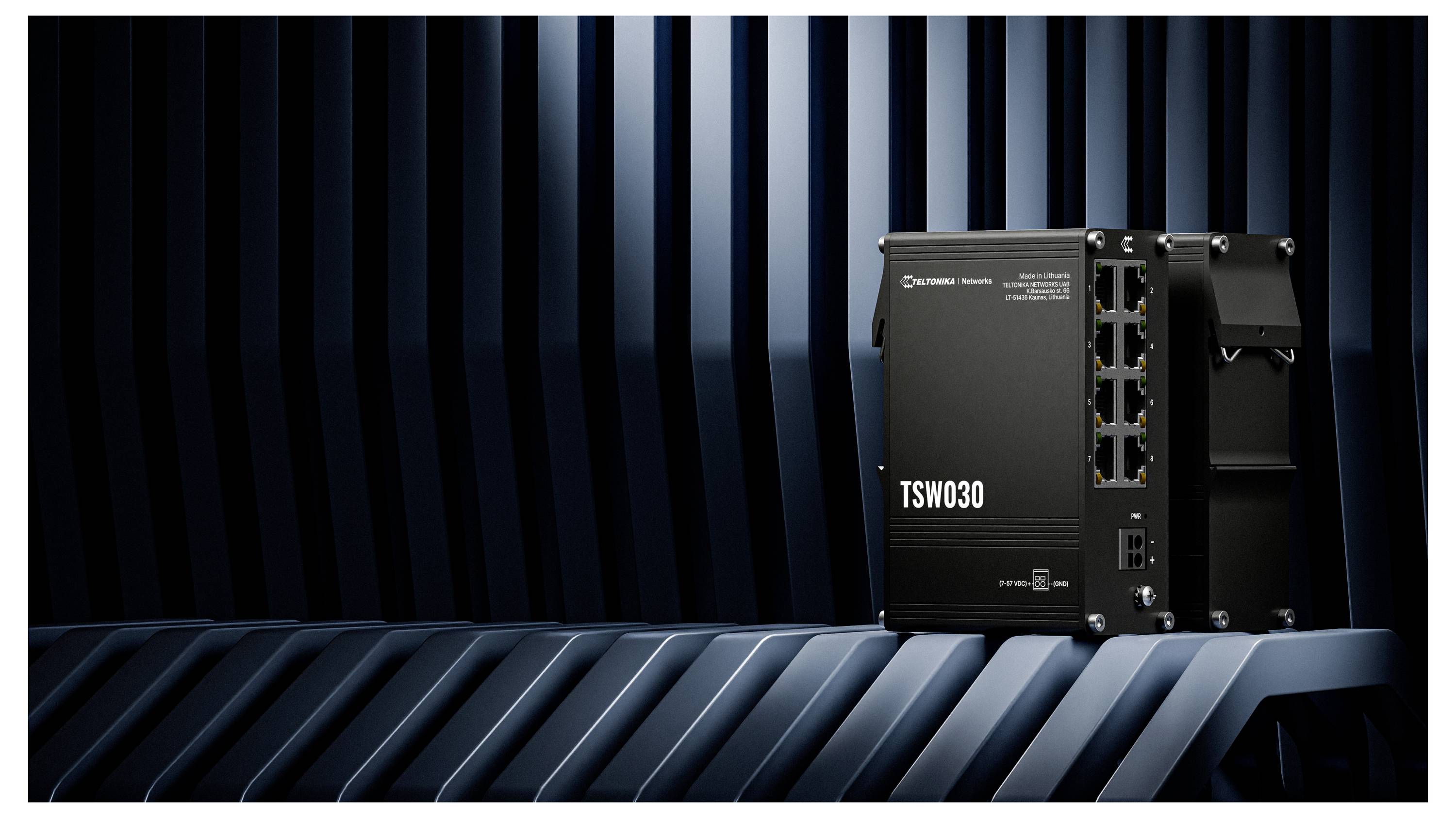 Un interruttore di rete TSW030 nero con cinque porte ethernet visibili si trova su una superficie metallica con uno sfondo di linee blu verticali.