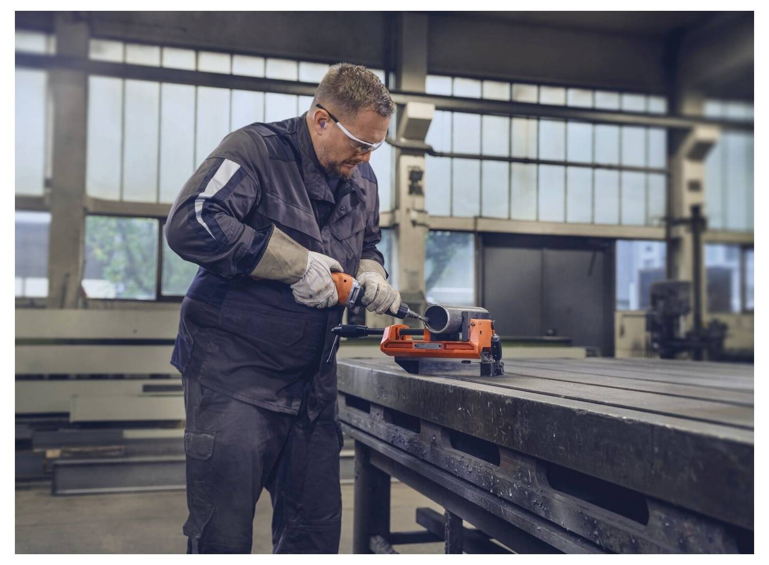 Un operaio in equipaggiamento protettivo taglia un tubo di metallo su una sega da banco industriale in un grande laboratorio.