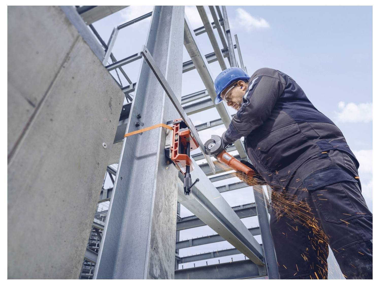 Un operaio edile con un casco blu e equipaggiamento di protezione utilizza una smerigliatrice per tagliare travi metalliche, con scintille che volano.