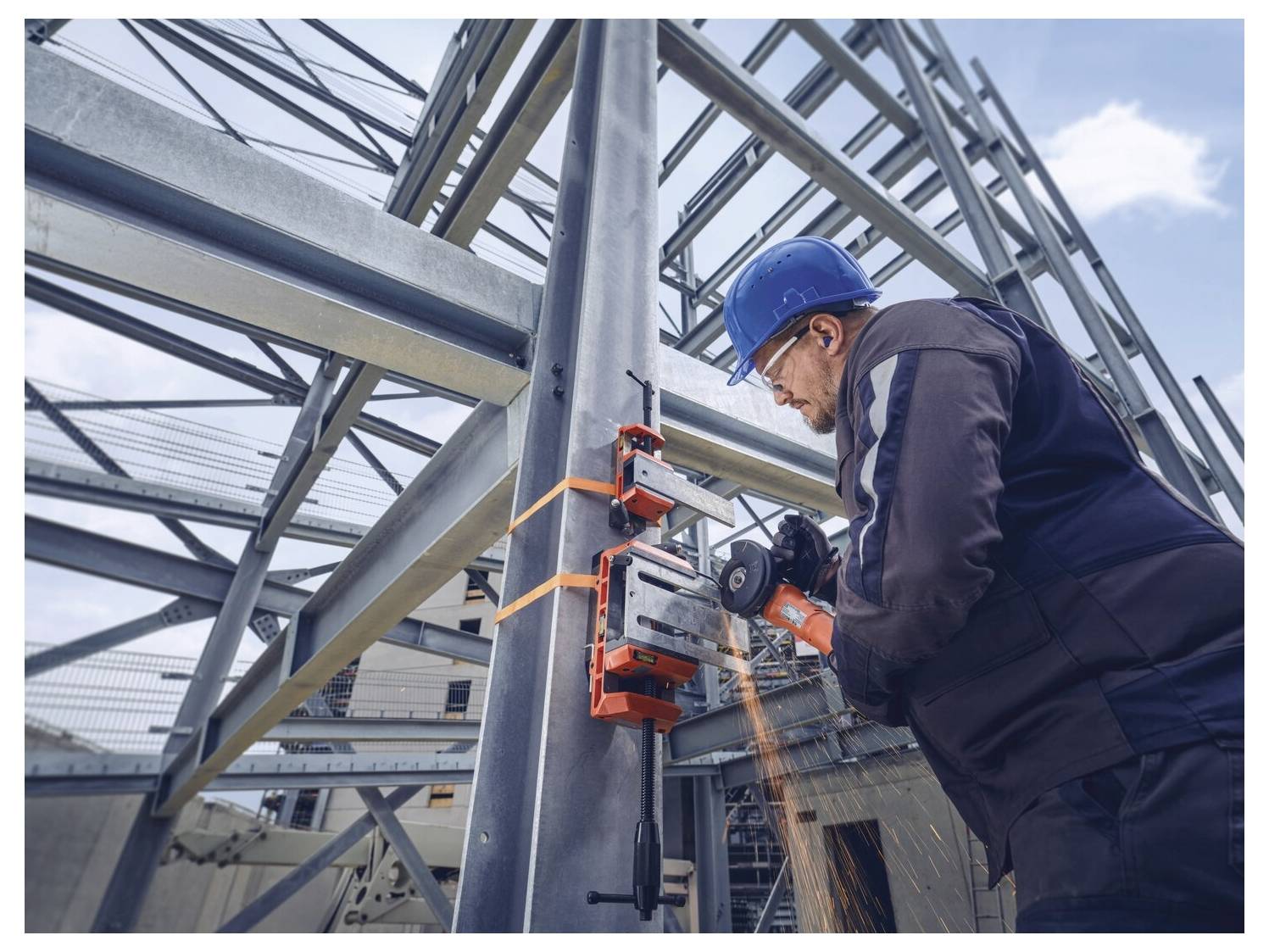 Un operaio edile che indossa un casco blu utilizza utensili elettrici per tagliare una trave d'acciaio su una struttura edilizia, con scintille che volano.