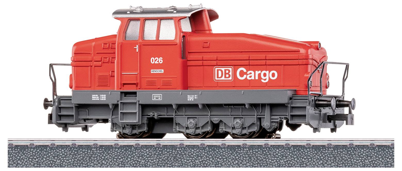 Un modello di treno merci rosso etichettato 'DB Cargo' con il numero '026' sul lato, esposto su una sezione di binario, che mostra una vista laterale.