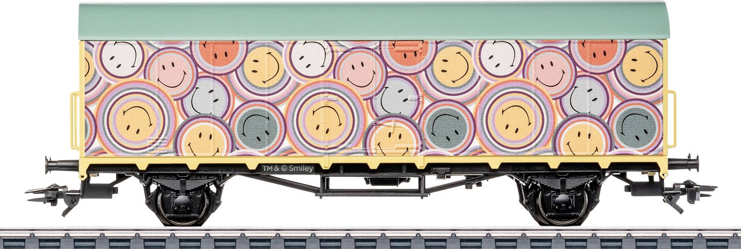 Un vagone ferroviario con faccine sorridenti colorate e motivi circolari. Il tetto è verde e il vagone è su un binario, visto da un lato.