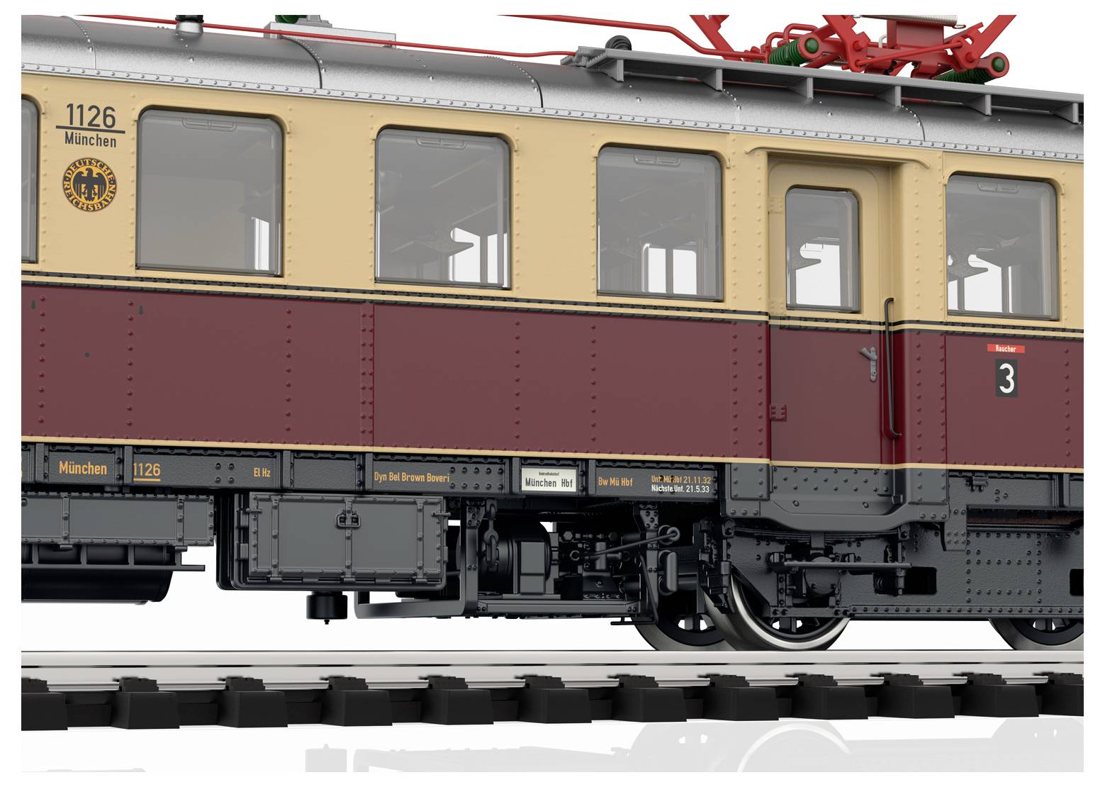 Un trenino in scala, dipinto di arancione e crema, viaggia lungo un binario ferroviario attraverso un paesaggio pittoresco con alberi e erba sullo sfondo.