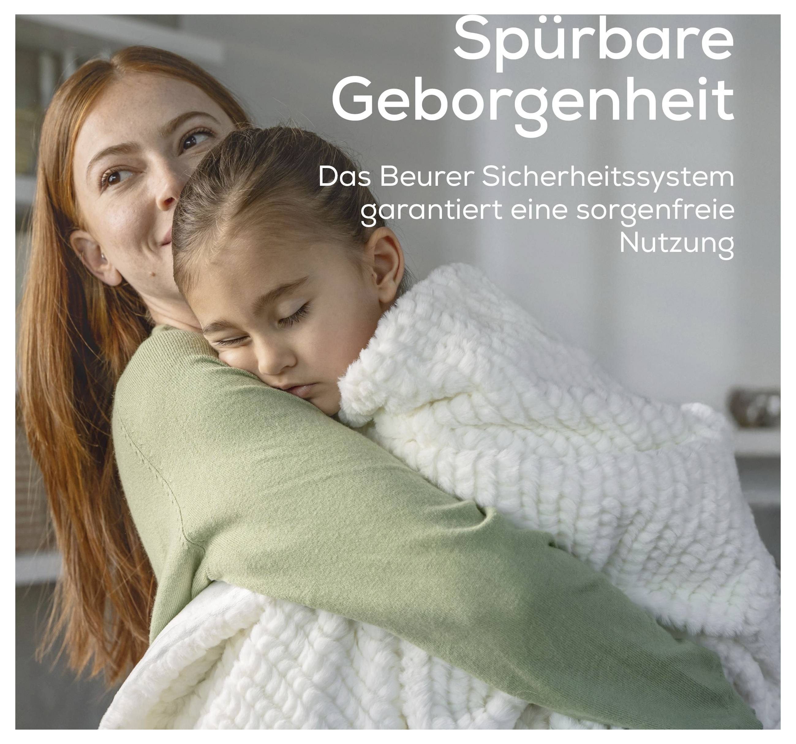 Una donna sorride mentre tiene in braccio un bambino addormentato avvolto in una coperta bianca. Il testo in tedesco recita: "Sicurezza tangibile. Il sistema di sicurezza Beurer garantisce un utilizzo senza preoccupazioni."