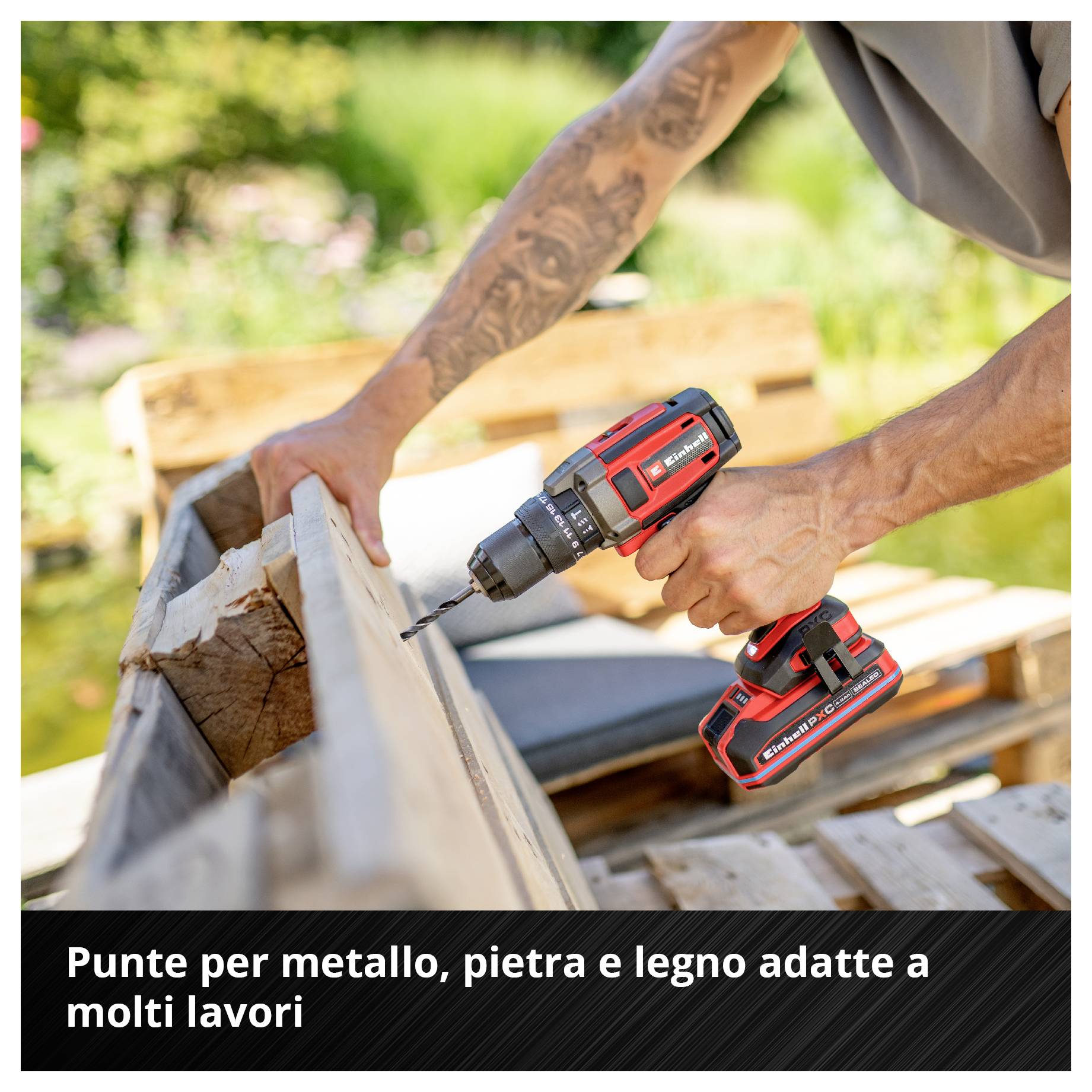 Un trapano a batteria rosso viene utilizzato da una persona per forare il legno. Sullo sfondo sono visibili mobili da giardino sfocati.