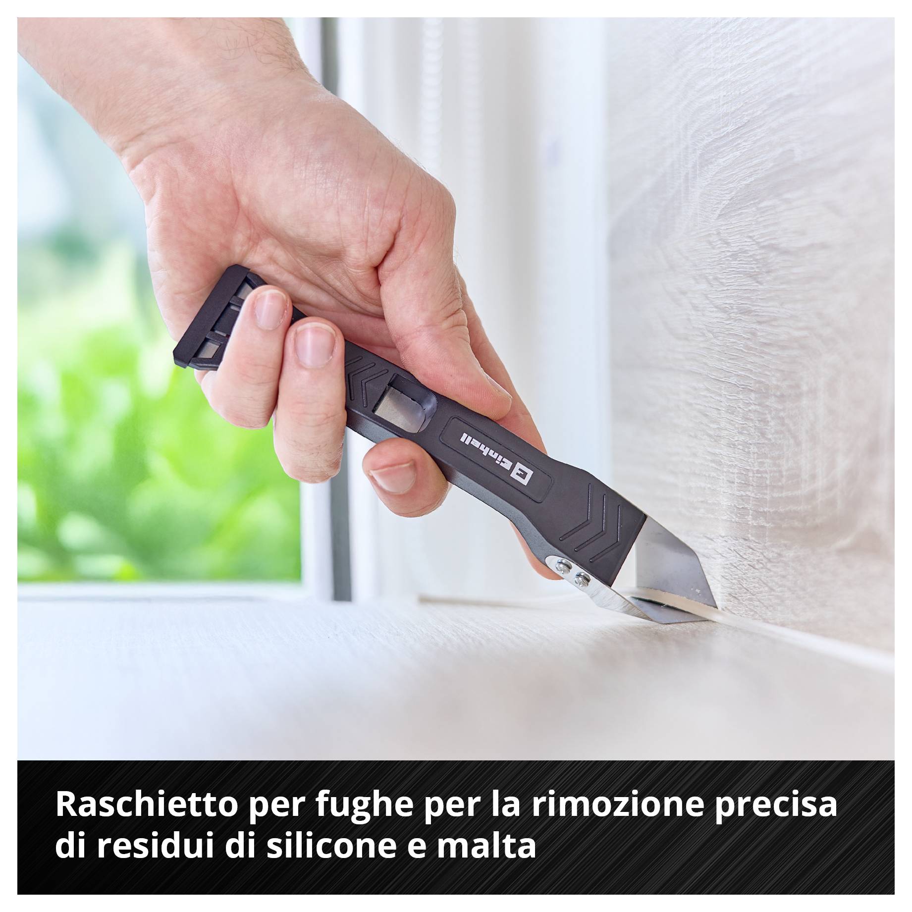 Mano che tiene un raschiafughe e rimuove i residui di silicone e malta da un bordo.