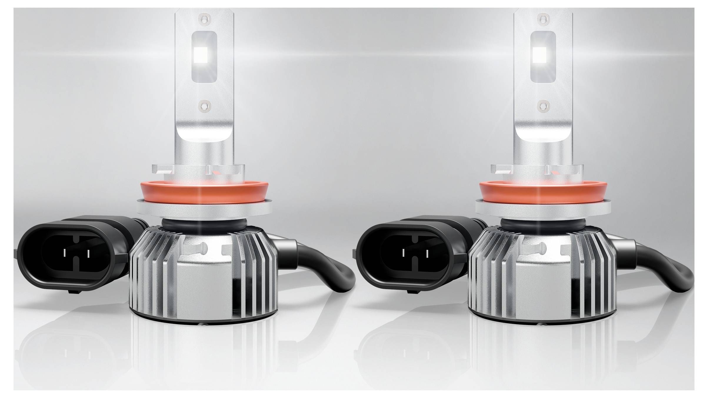'Due lampadine per fari LED con dissipatori di calore argentati e connettori neri, posizionate fianco a fianco su una superficie riflettente.'