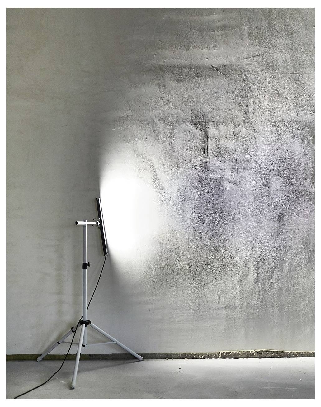 Una lampada da terra illumina un muro bianco con texture in una stanza minimalista, evidenziando la sua superficie ruvida e le ombre sottili.