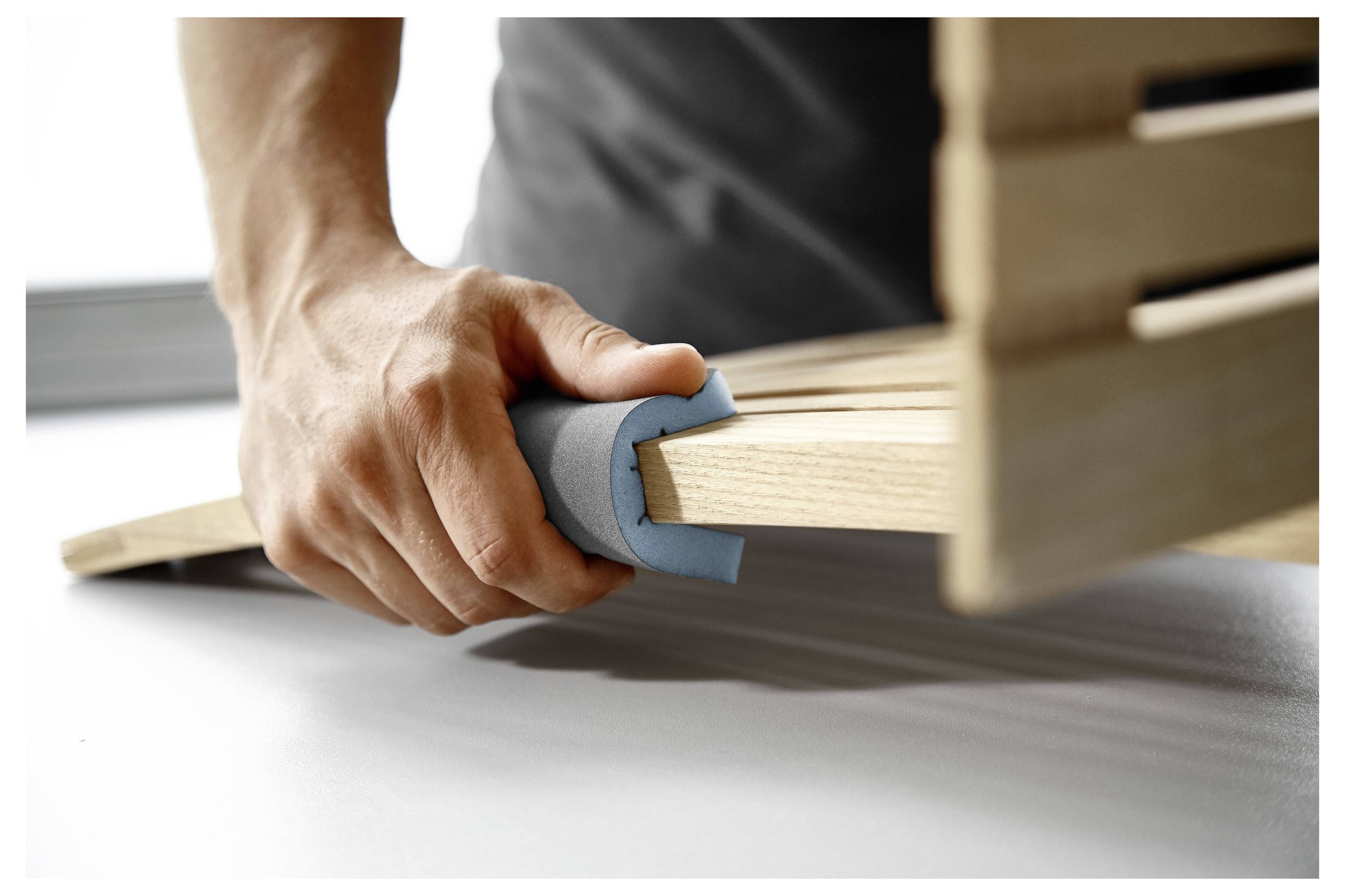 Una persona sta applicando un protettore in schiuma blu ai bordi di una tavola di legno per motivi di sicurezza.