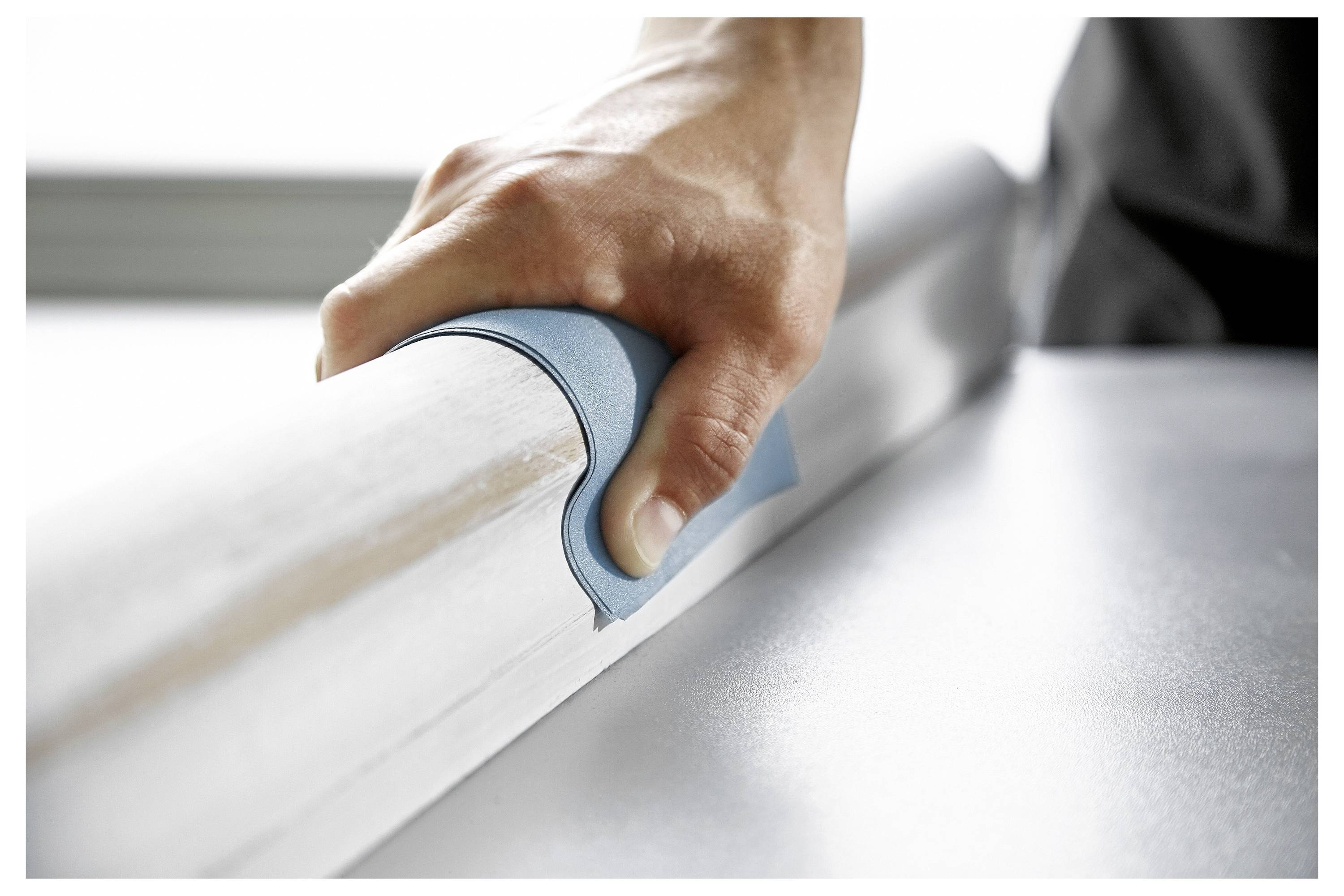 Una mano che utilizza un tampone abrasivo blu per carteggiare una superficie metallica, concentrandosi sulla levigatura e sulla finitura.