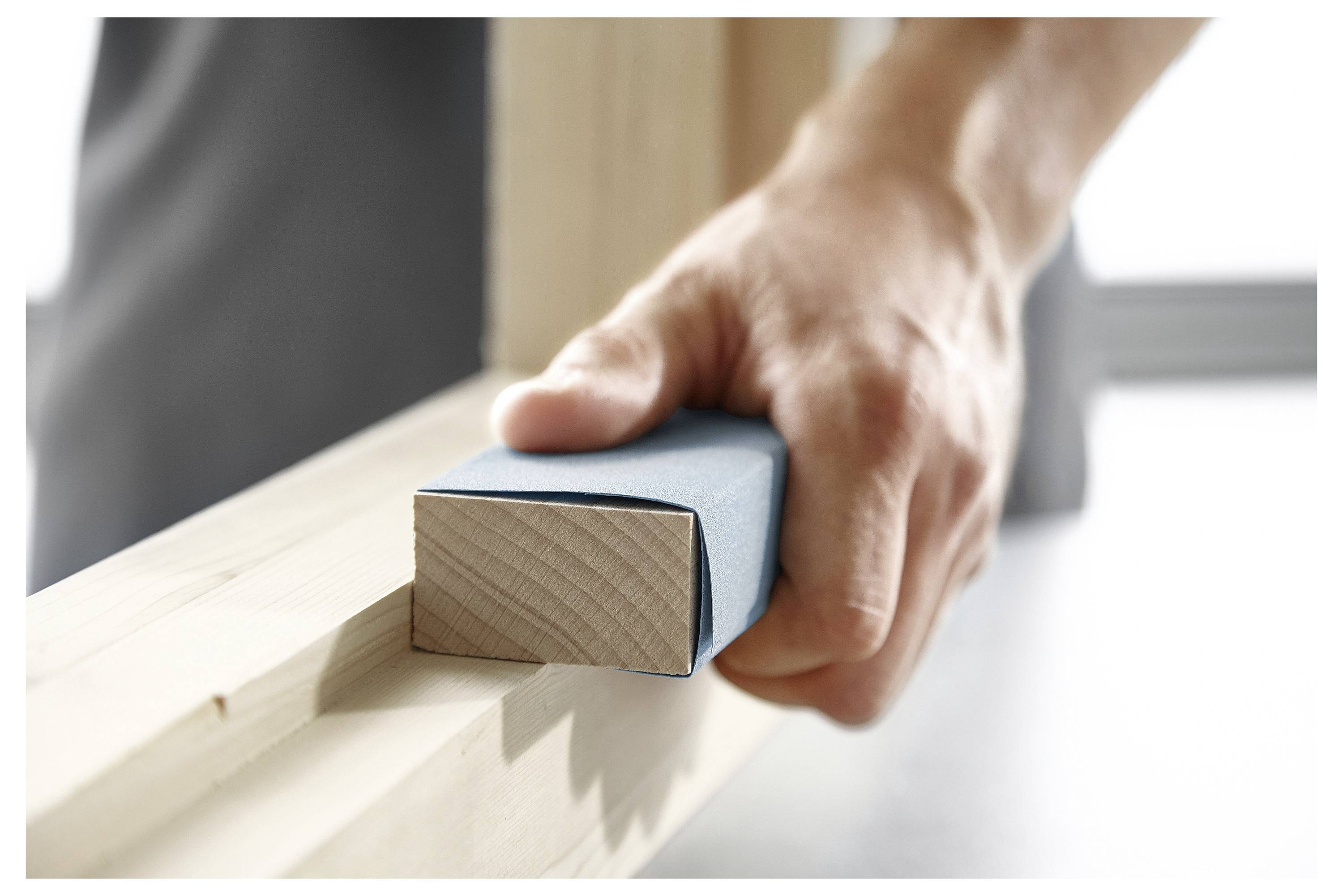 Una mano utilizza carta vetrata per levigare una superficie di legno, evidenziando l'artigianato della lavorazione del legno.