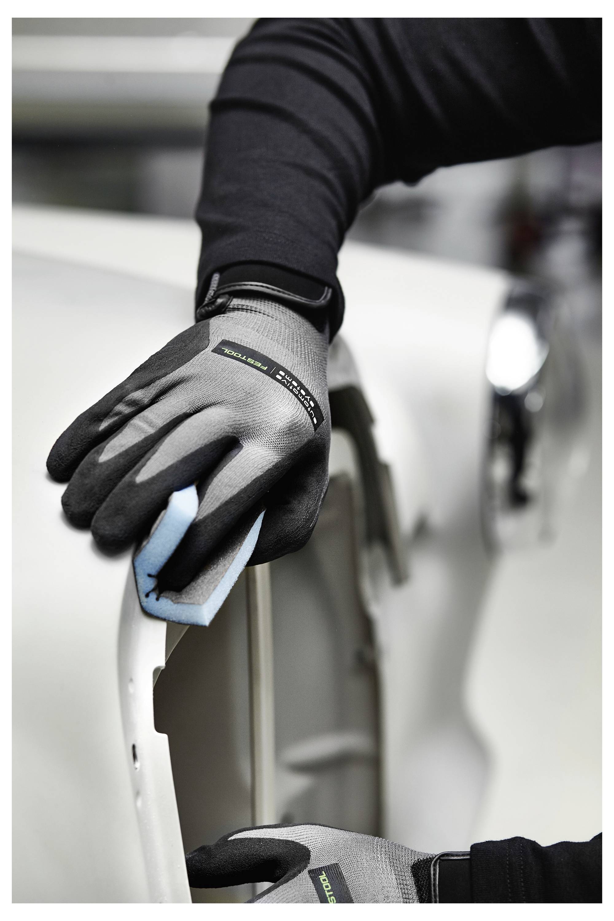 Una persona che indossa guanti pulisce l'esterno di un'auto con una spugna blu, concentrandosi sulla superficie del veicolo di colore chiaro, evidenziando i dettagli della cura.