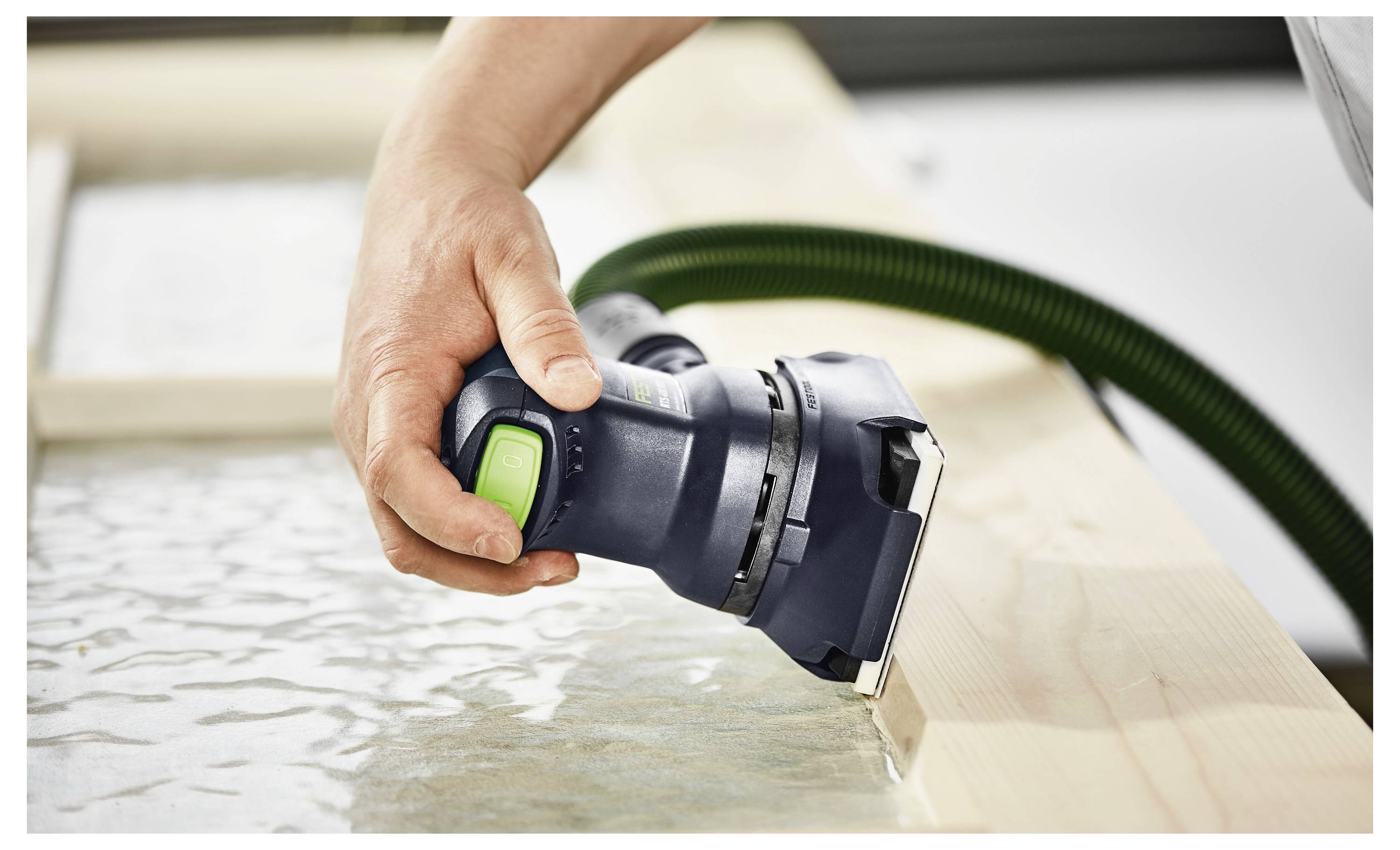 Una persona che tiene in mano una levigatrice elettrica e un rivestimento protettivo mentre leviga una superficie di legno, concentrandosi sull'artigianato e sulla sicurezza.