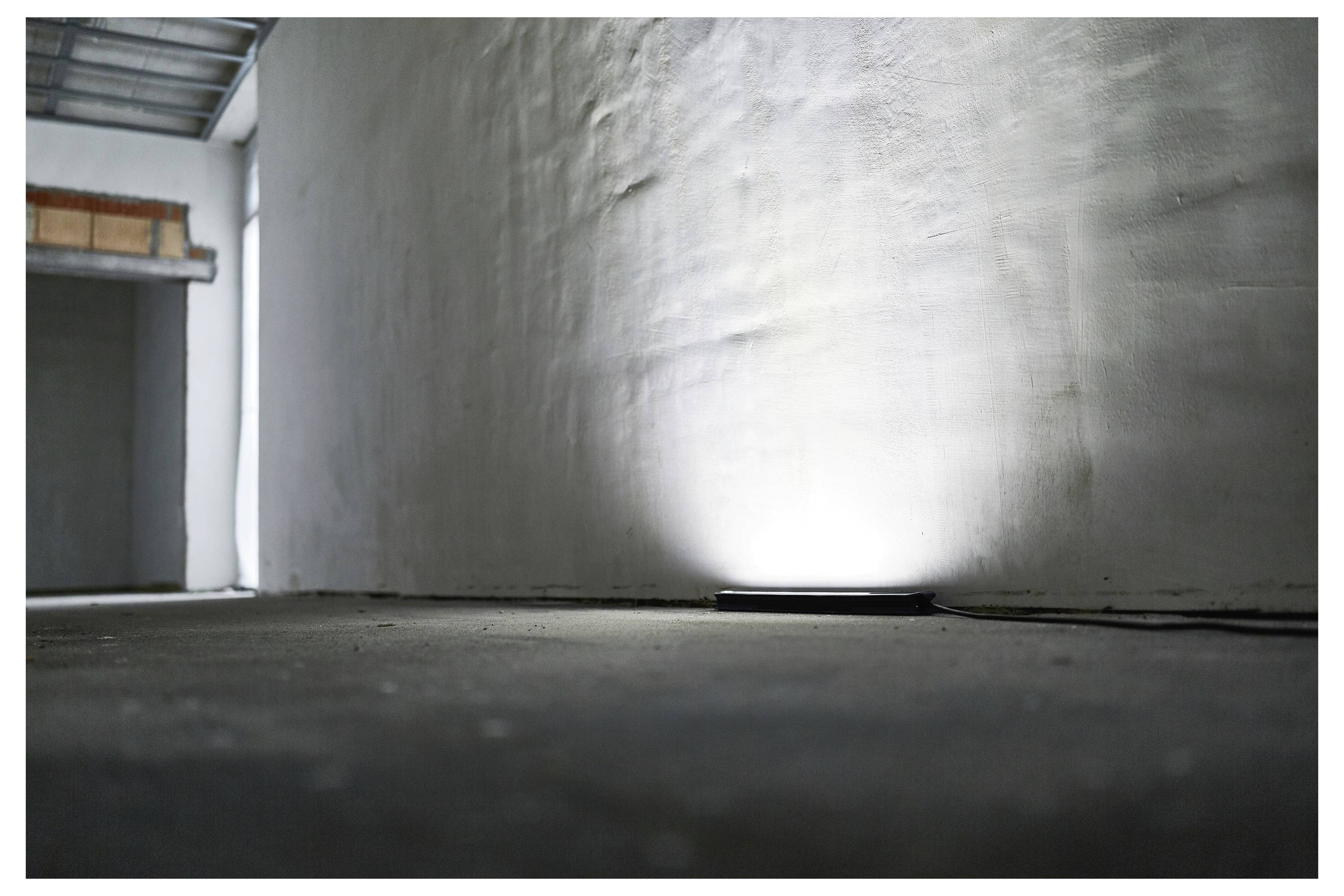 Una stanza scarsamente illuminata e vuota con un riflettore sul pavimento che illumina un muro con texture.
