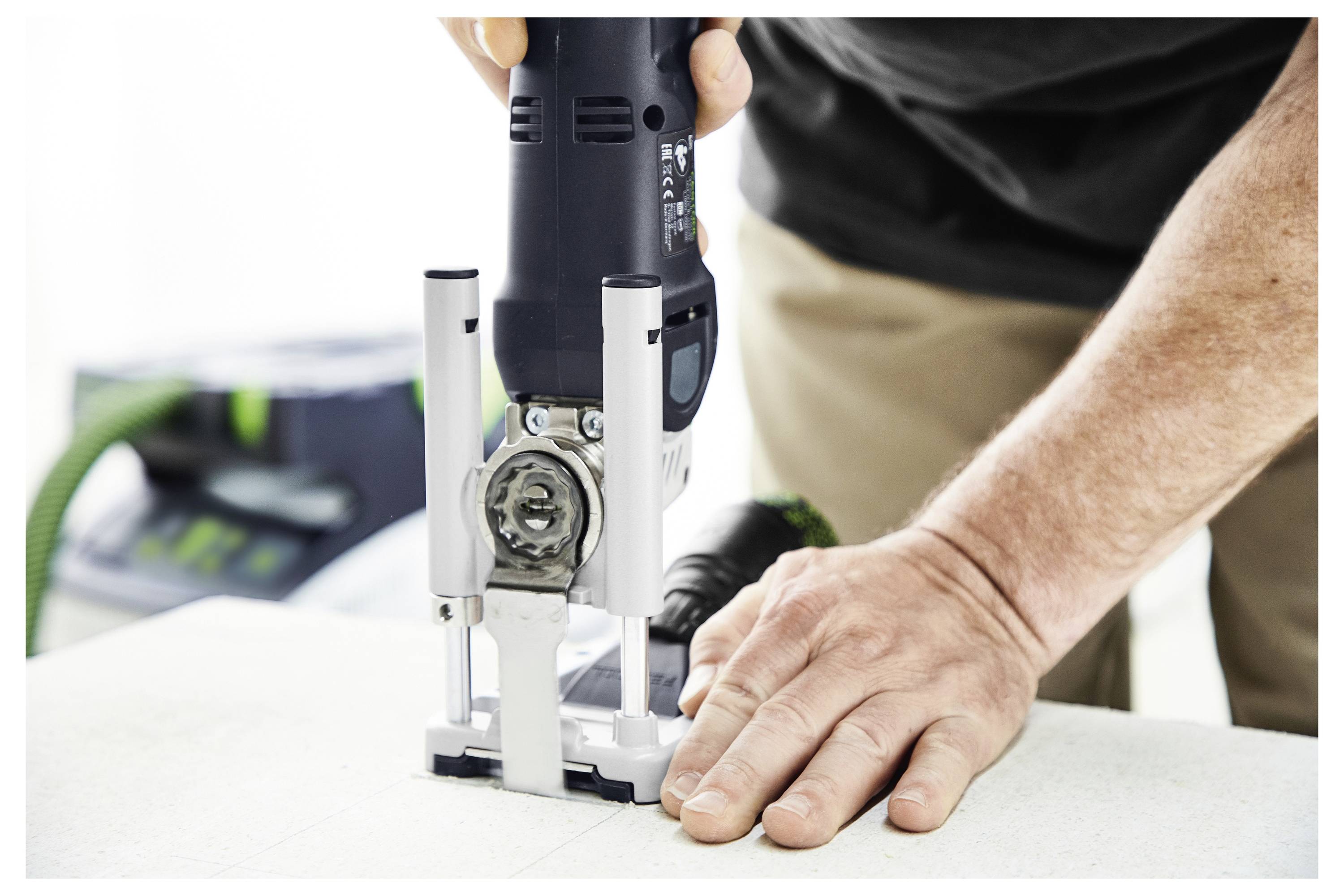 Una persona utilizza un utensile elettrico per tagliare del materiale su un tavolo, con un sistema di aspirazione in background per l'estrazione della polvere.