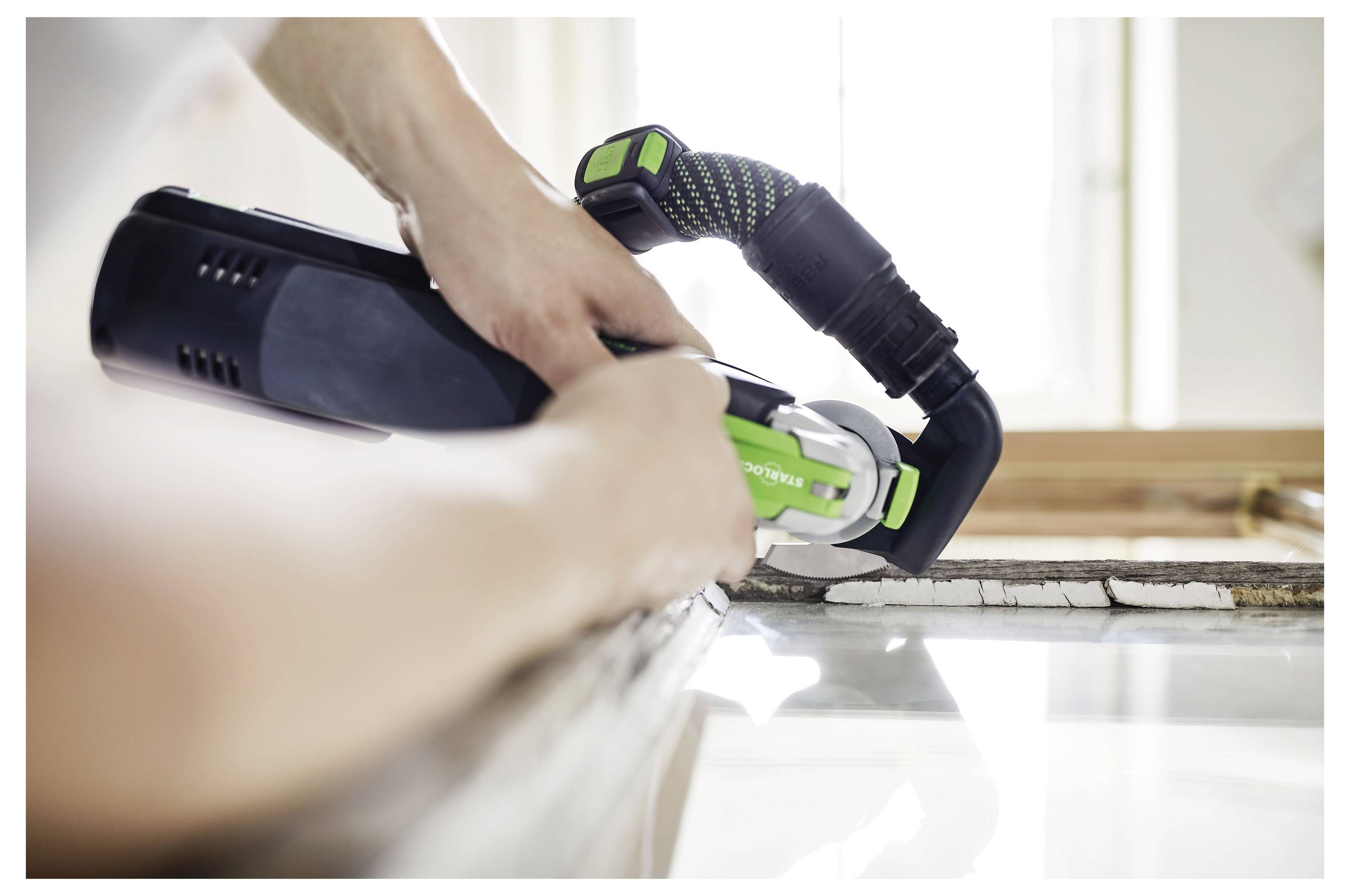 Una persona sta regolando una levigatrice elettrica con un disco circolare blu, collegata a un estrattore di polvere Festool. Sta preparandosi per la levigatura.