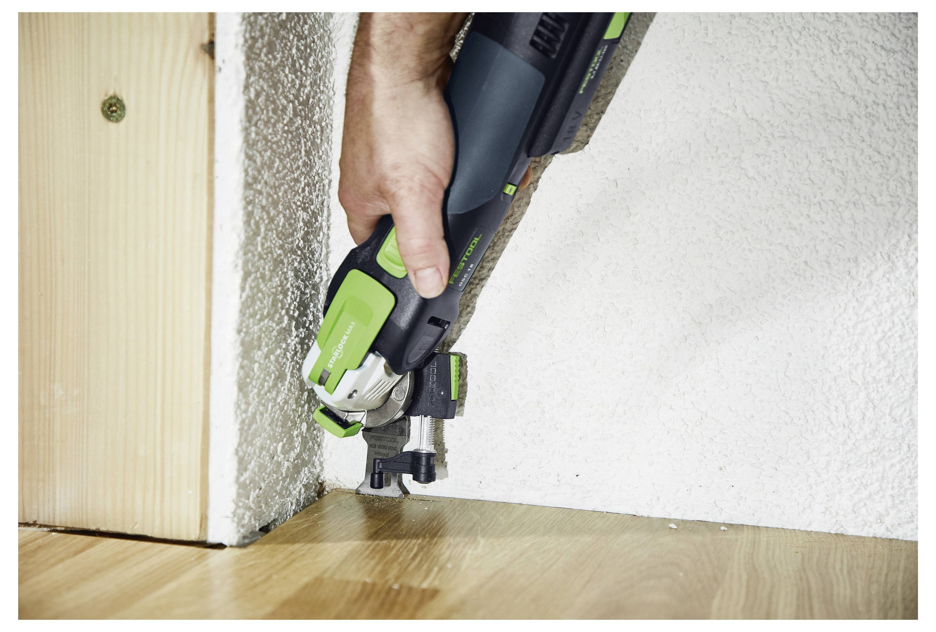 Una persona utilizza un attrezzo elettrico per tagliare un pannello di legno vicino a un muro, dimostrando un'attività di fai da te o di costruzione.