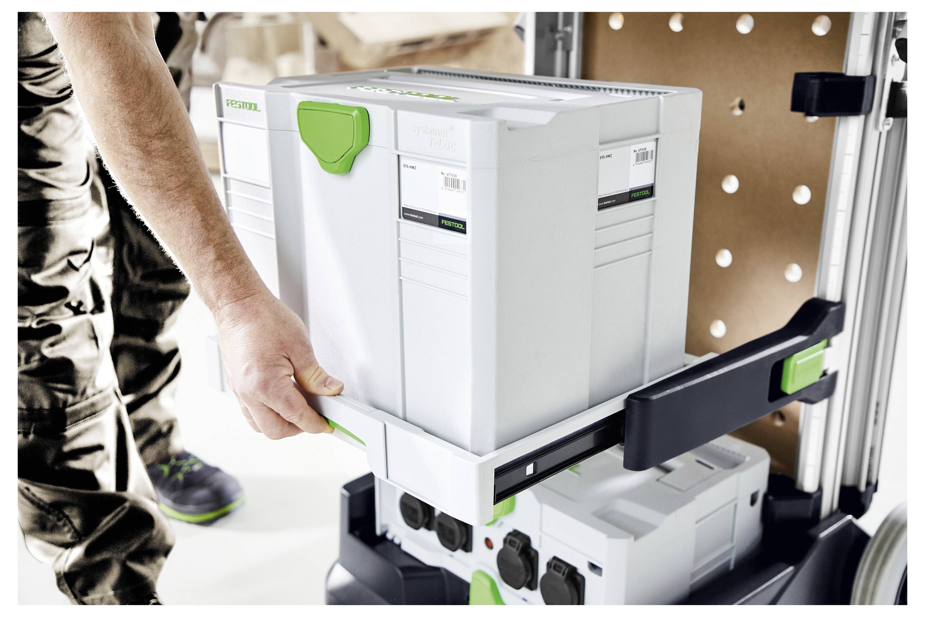 Una persona indossando abbigliamento da cantiere mescola il materiale in un grande secchio all'interno di una stanza parzialmente ristrutturata con pareti in mattoni a vista e attrezzi da lavoro.