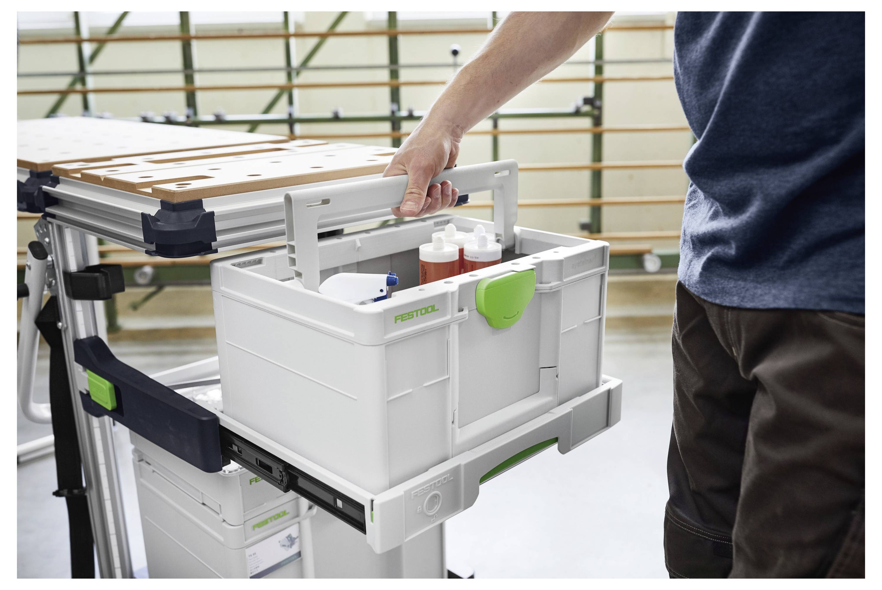 Una persona estrae un cassetto con attrezzi da un banco da lavoro, rivelando bottiglie e attrezzi organizzati. L'ambiente sembra essere un laboratorio artigianale.