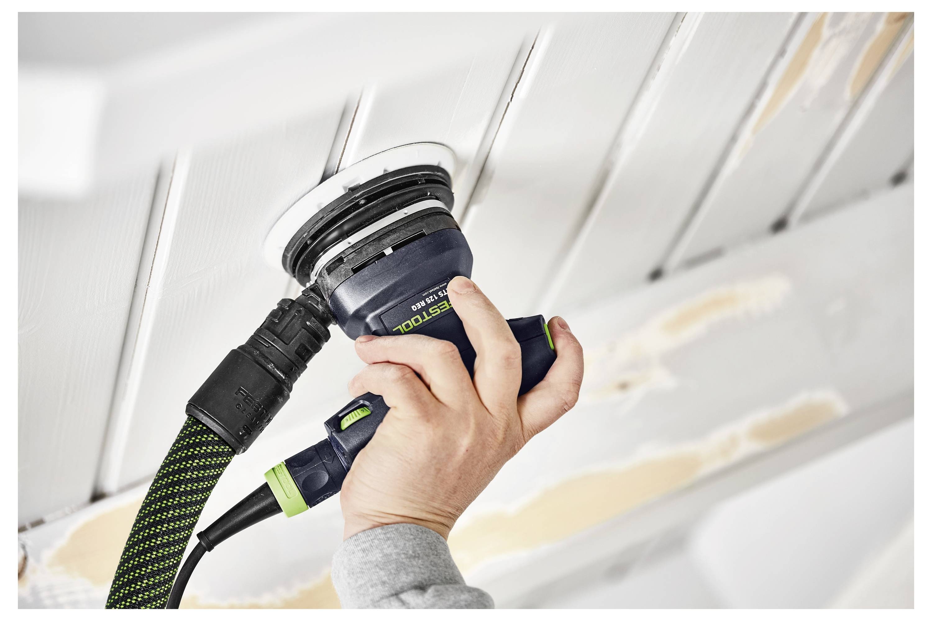 Una persona utilizza una levigatrice elettrica portatile su un soffitto in legno, levigando la superficie. Il soffitto presenta notevoli differenze di texture.