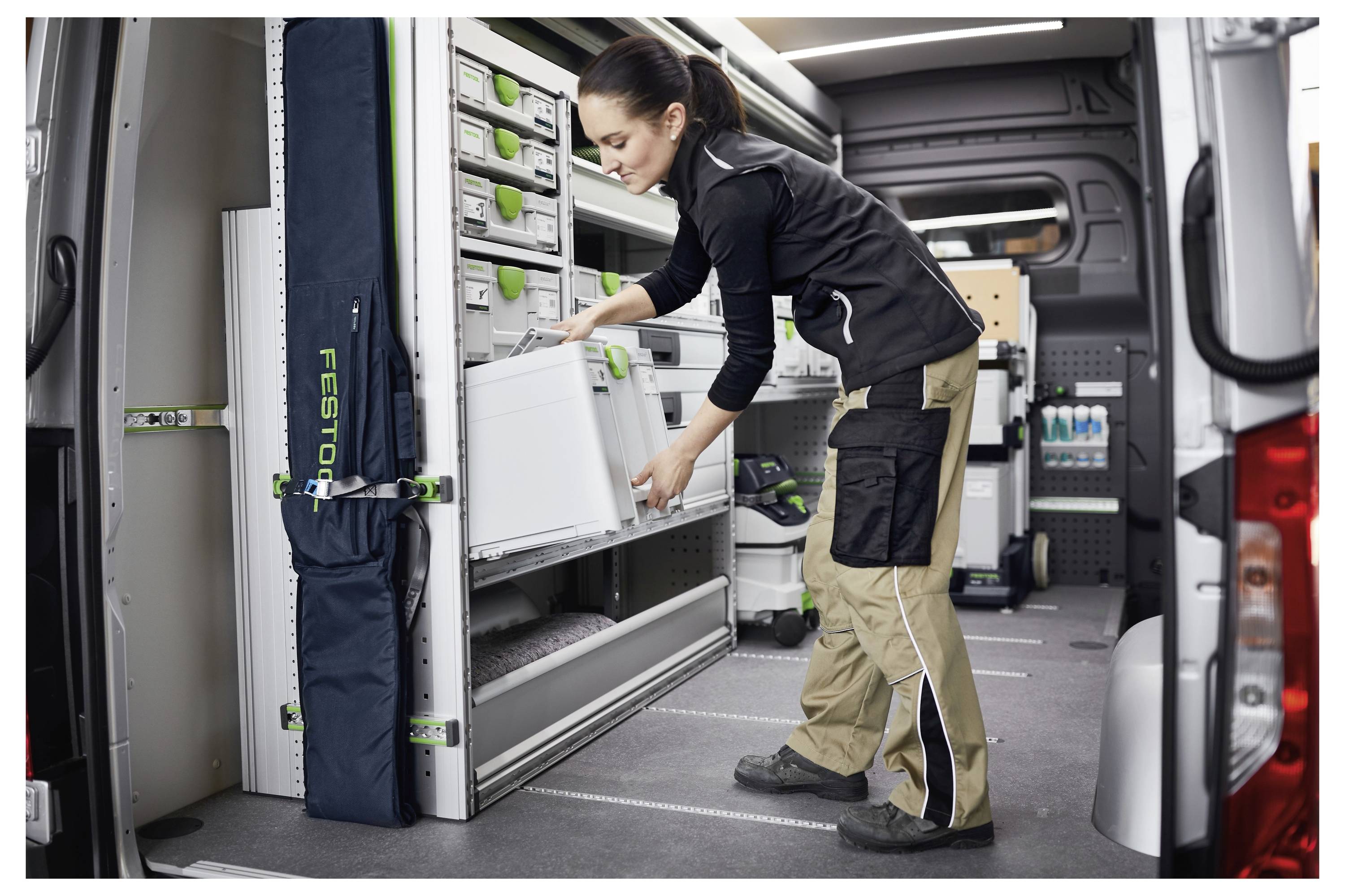 Una persona organizza attrezzi e attrezzature all'interno di un furgone di servizio ben attrezzato con scaffali e spazi di archiviazione, garantendo un accesso efficiente e un flusso di lavoro ottimale.