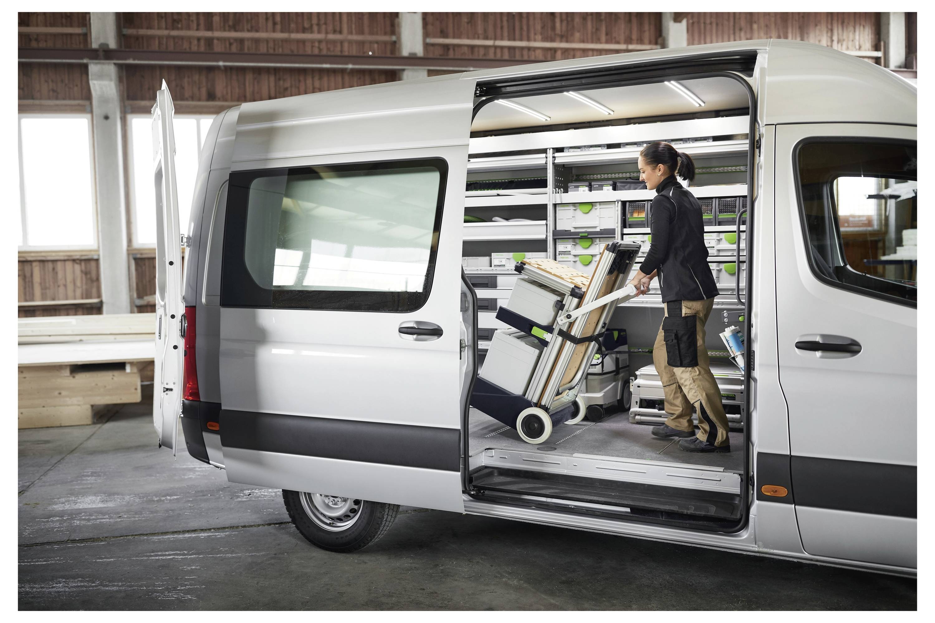 Una persona organizza l'equipaggiamento all'interno di un furgone con porta scorrevole aperta, mostrando un sistema di stoccaggio con scaffali e attrezzi.