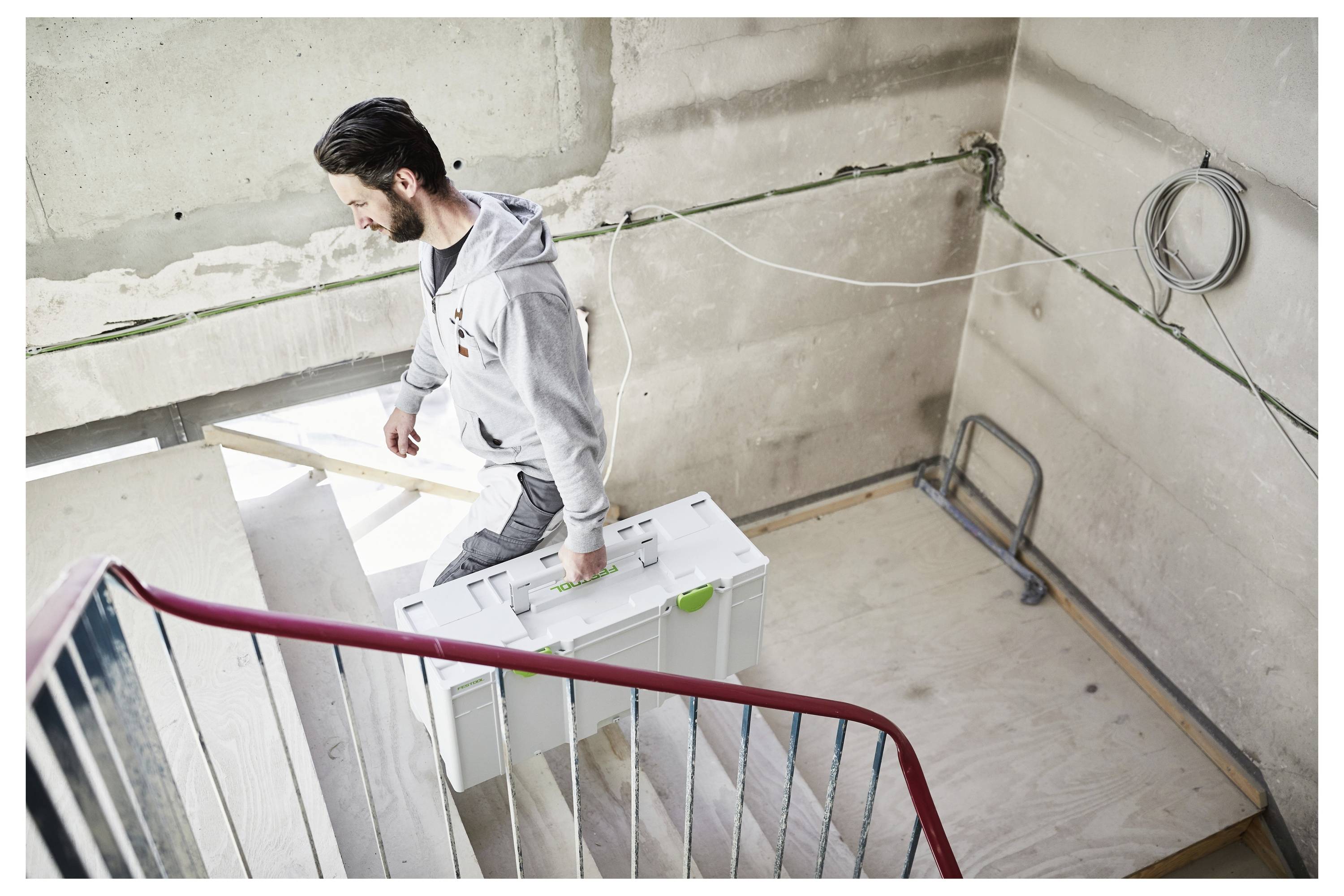 Uomo che trasporta una grande scatola bianca su una scalinata in cemento in un edificio incompiuto, suggerendo lavori di costruzione o ristrutturazione.