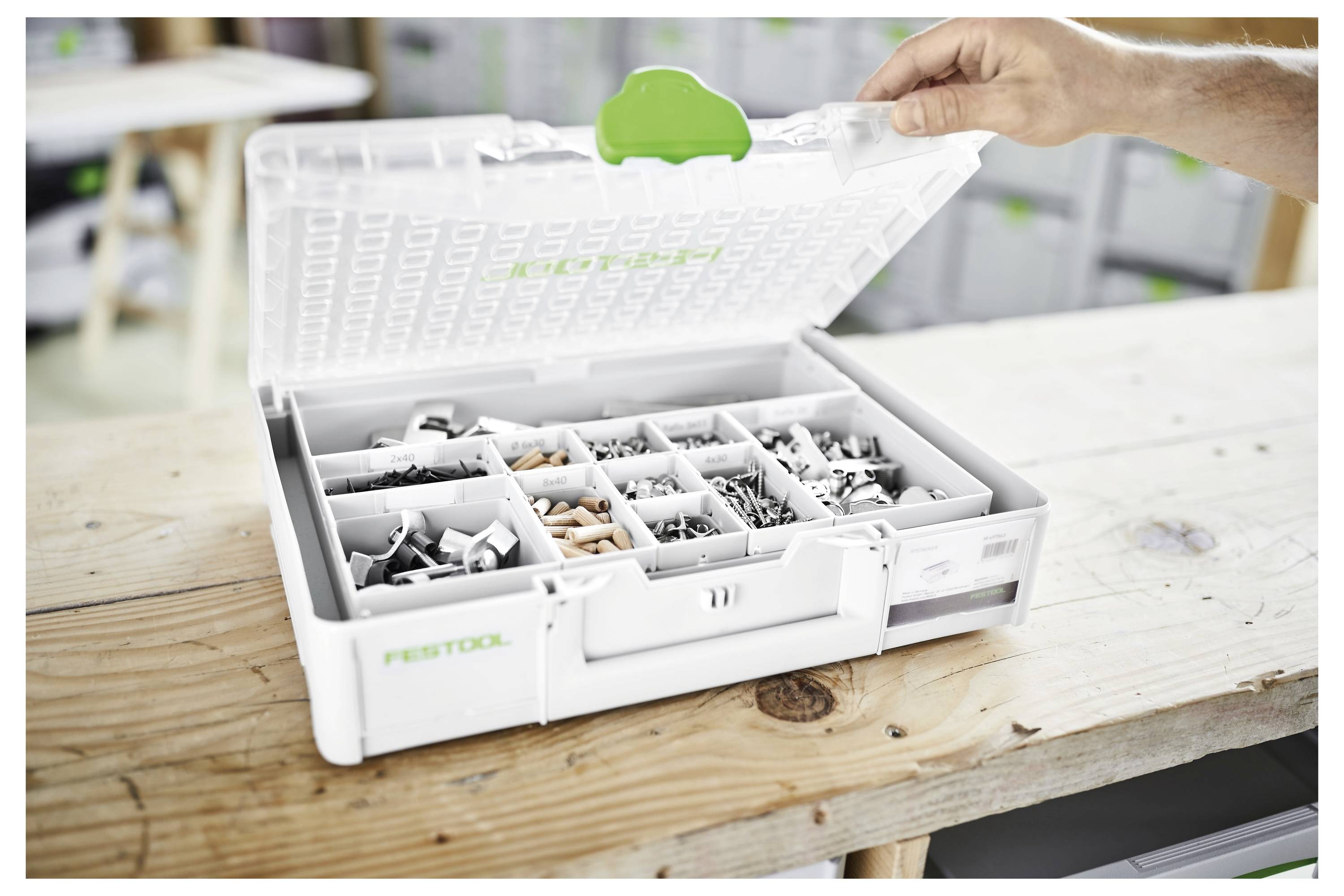 Una persona che indossa una giacca scura tiene in mano un contenitore di plastica trasparente con un coperchio bianco, suggerendo organizzazione o conservazione in un ambiente domestico o d'ufficio.