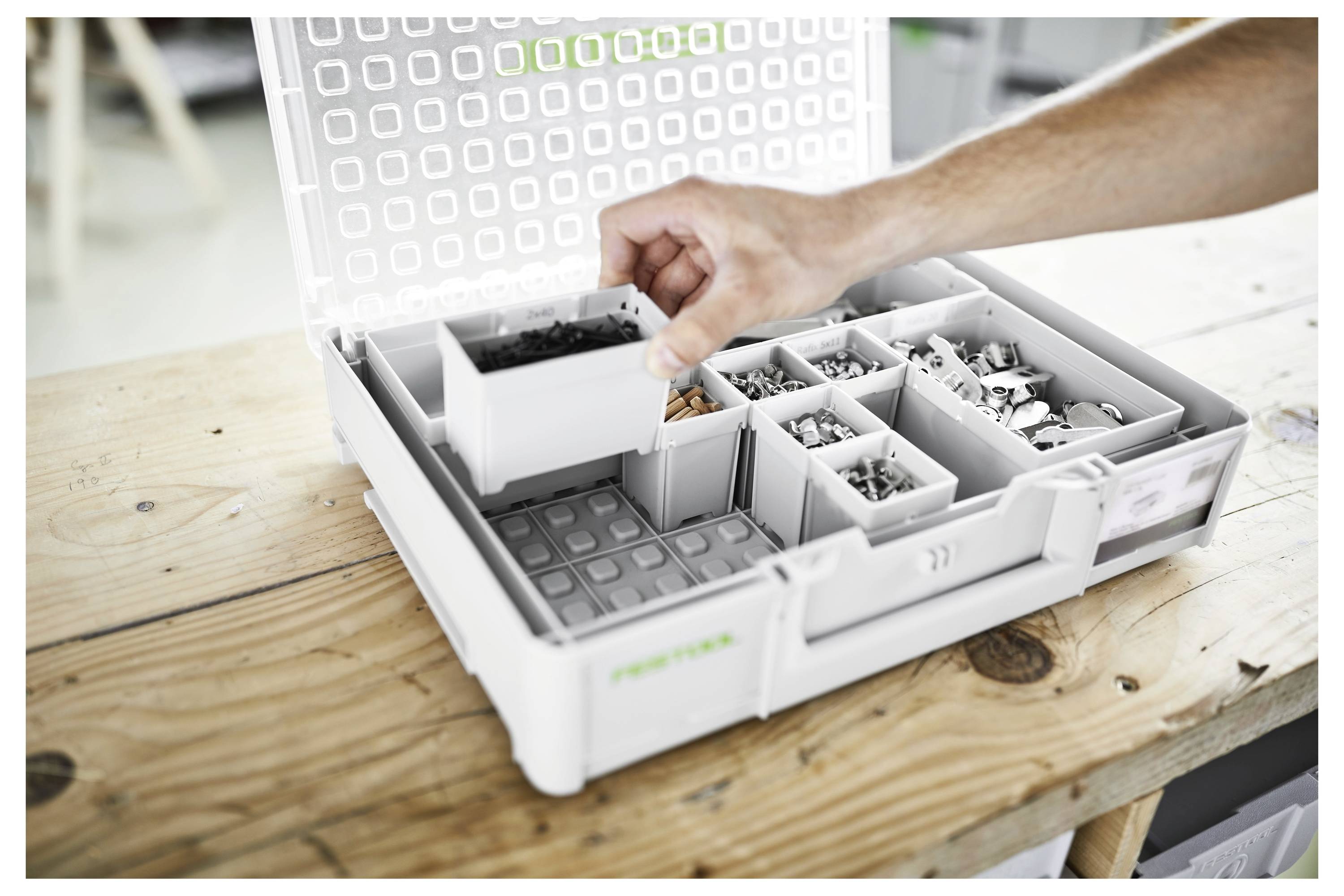 Una persona organizza vari piccoli componenti hardware in una scatola di immagazzinamento in plastica con scomparti regolabili su un tavolo di legno.