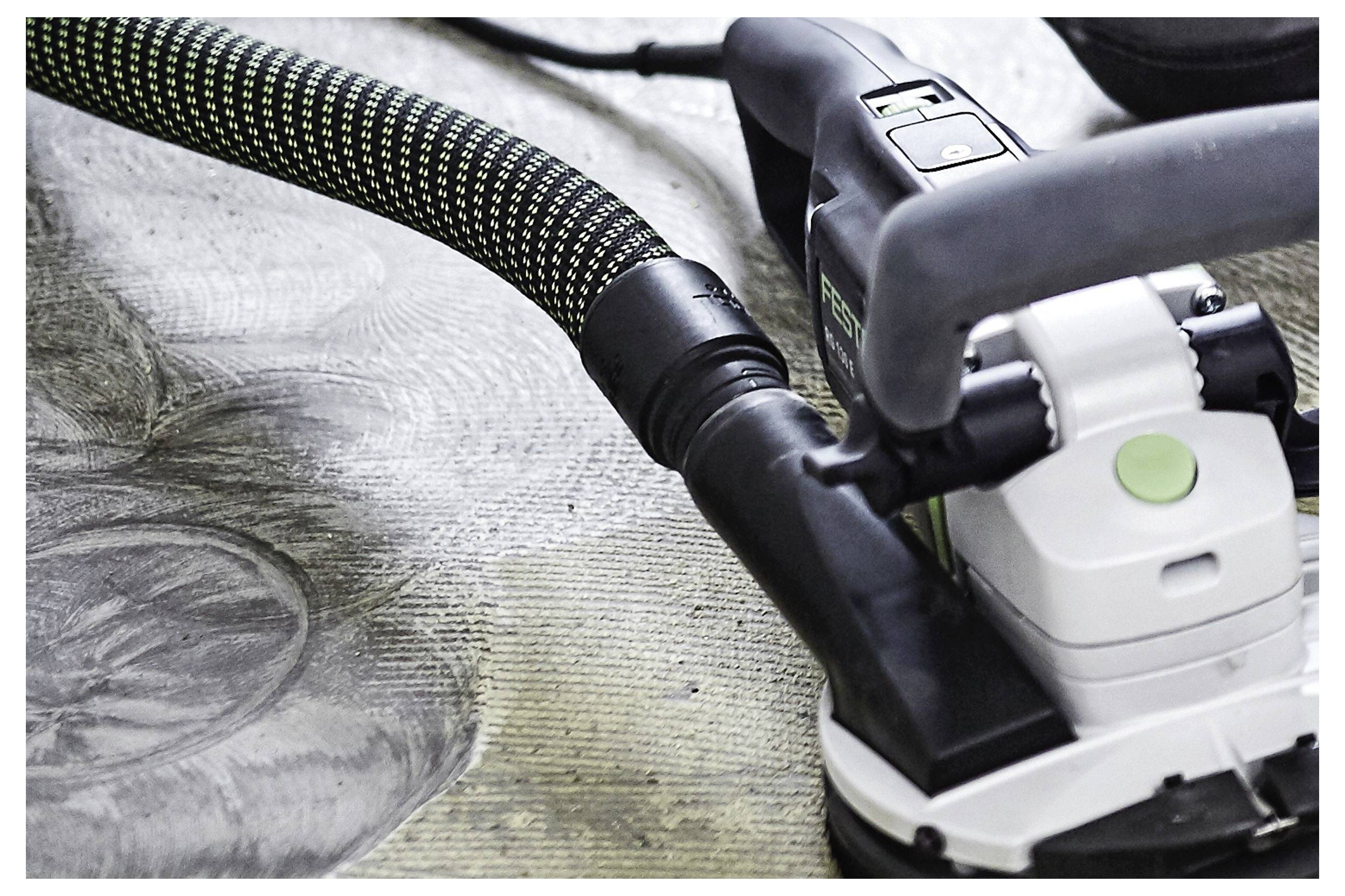 Un primo piano di una levigatrice elettrica con un tubo di aspirazione della polvere collegato, che leviga una superficie di legno. La venatura e i motivi del legno sono visibili.